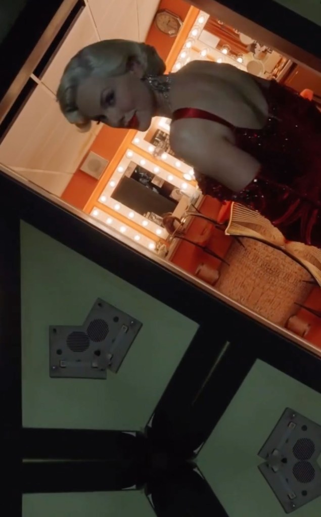 Taylor Swift dressed as Marilyn Monroe, wearing a red sequined dress and silver necklace, seen from a high angle looking down into a green-tinted reflected surface.