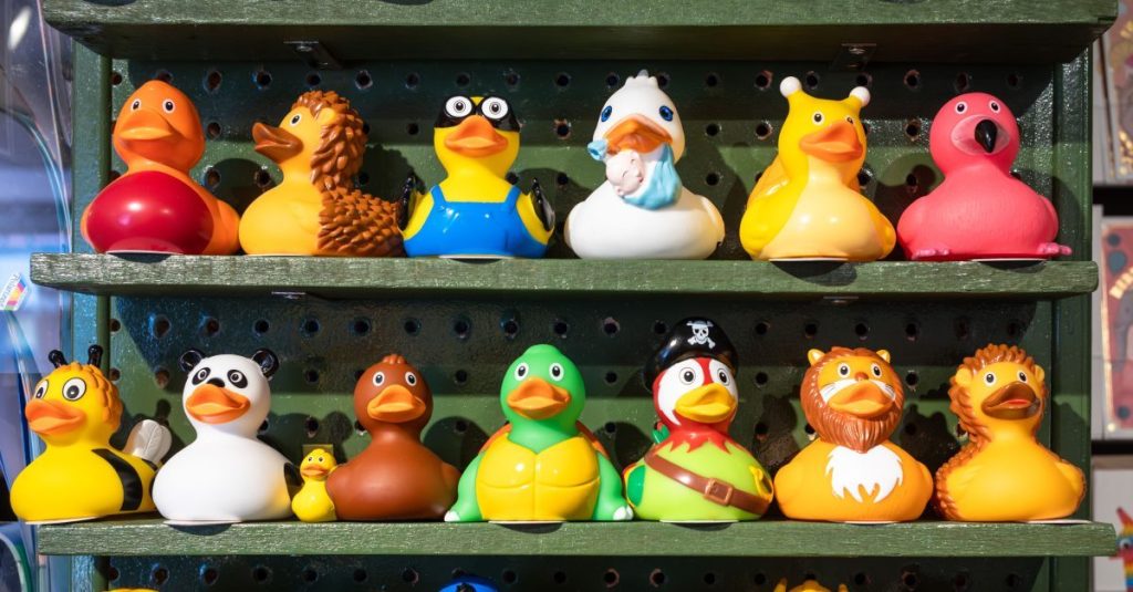 20 fun and colorful rubber ducks in different disguises including as superheroes lined up in three rows on shelves in a shop in Brighton, East Sussex, UK