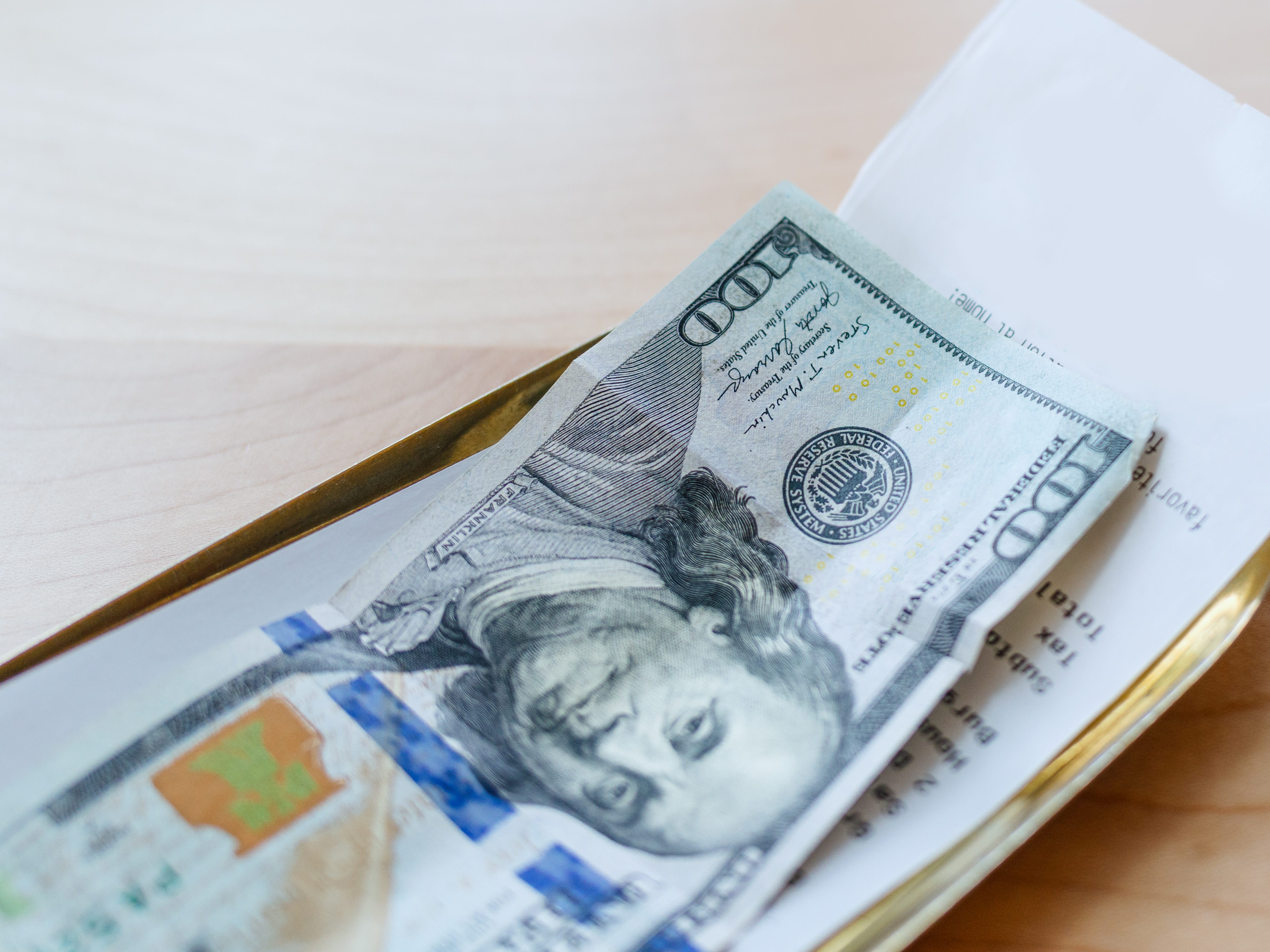 A $100 bill on top of a check at a restaurant.