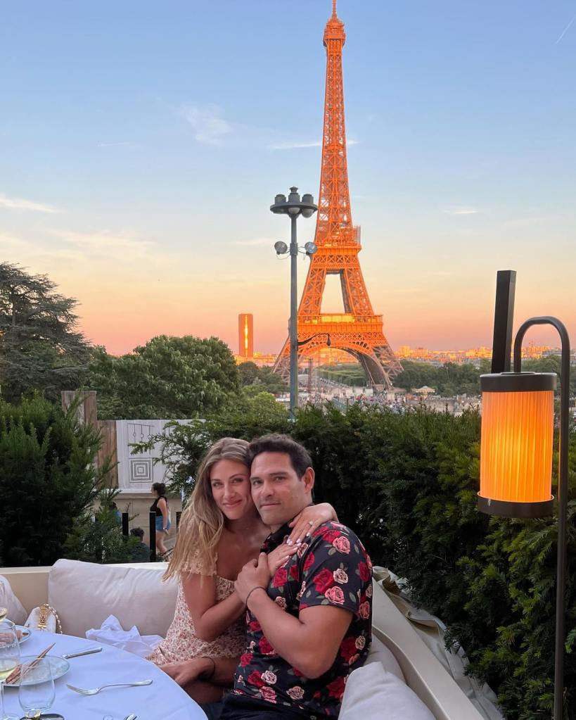 Mark Sanchez and Perry Mattfeld posing together with the Eiffel Tower in the background at sunset.