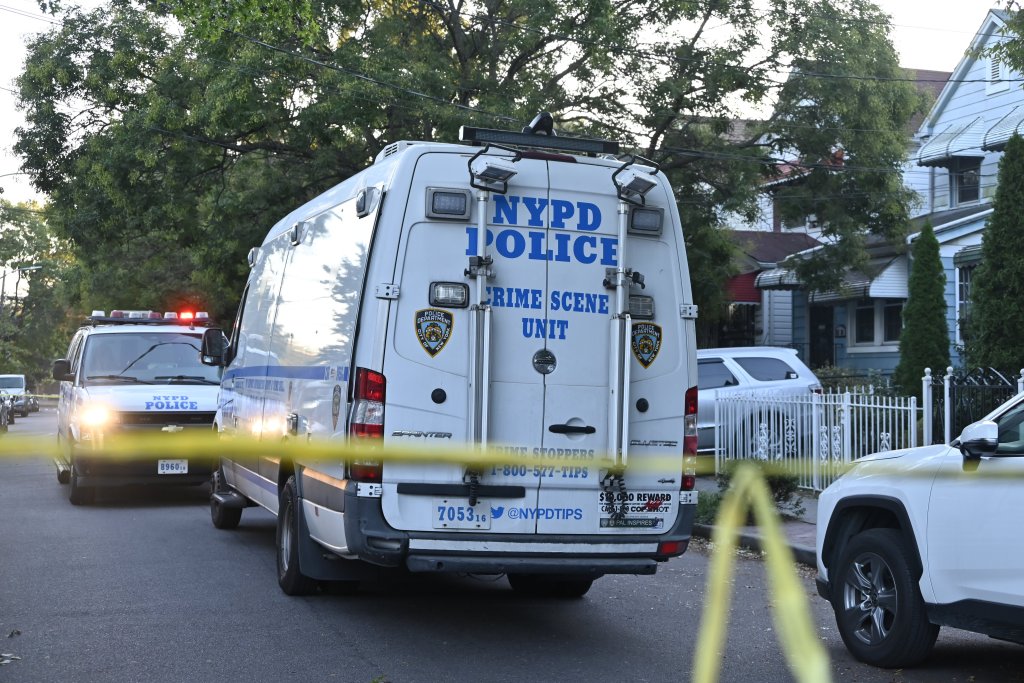 NYPD police and crime scene unit vans with flashing lights behind yellow crime scene tape.