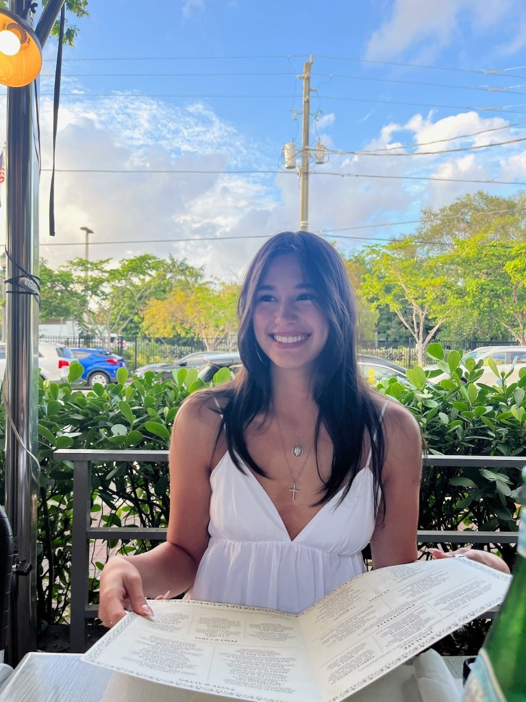 Krysta Tsukahara smiling and holding a menu at an outdoor restaurant.