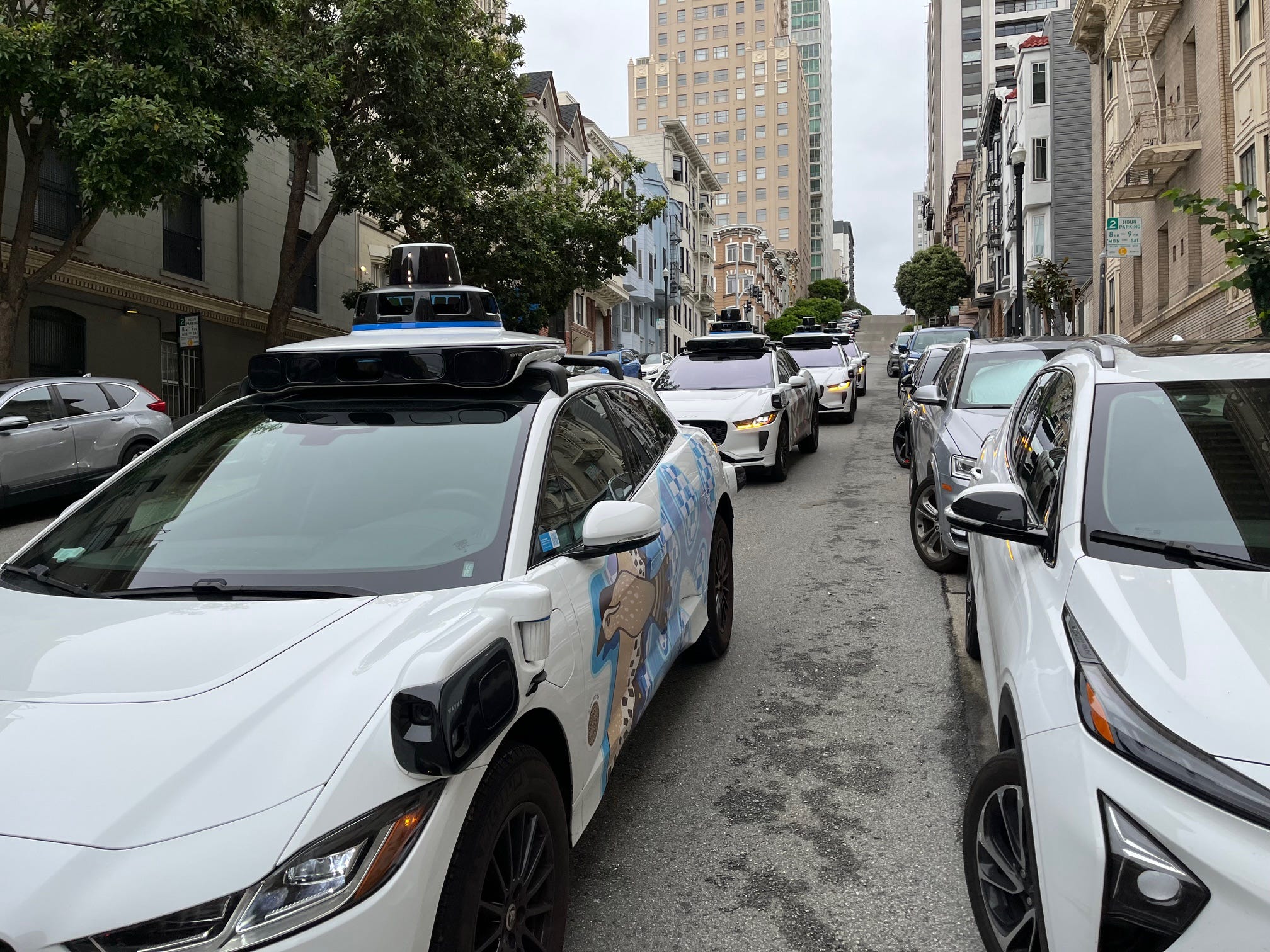 Four Waymo cars sit stopped on a street in San Francisco.