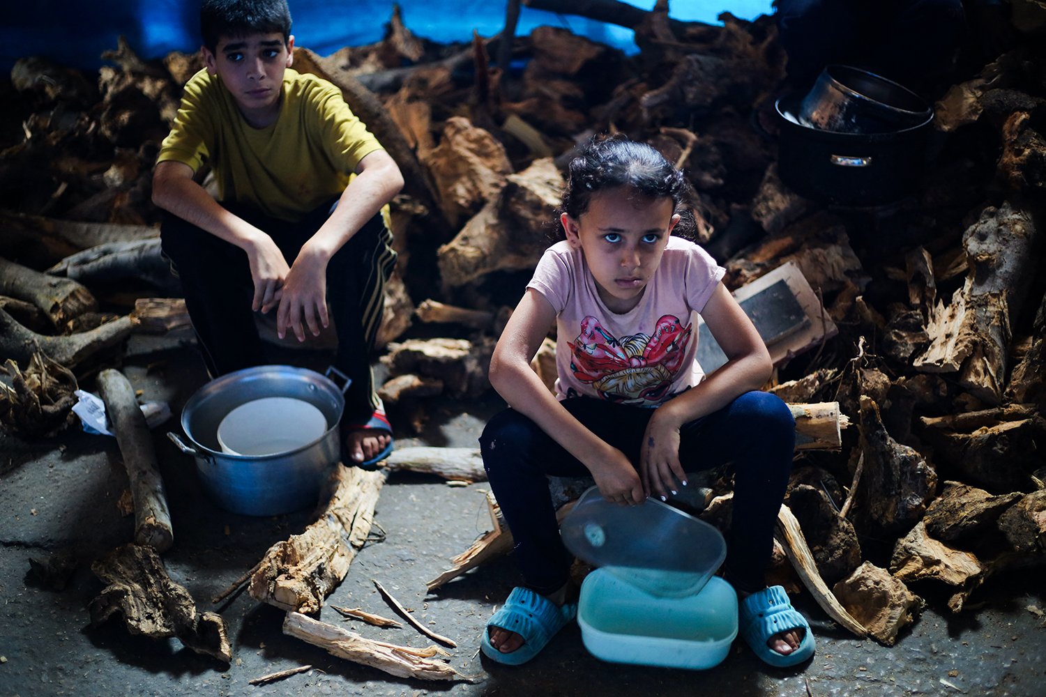 Children sit on the ground with empty bowls in front of them.