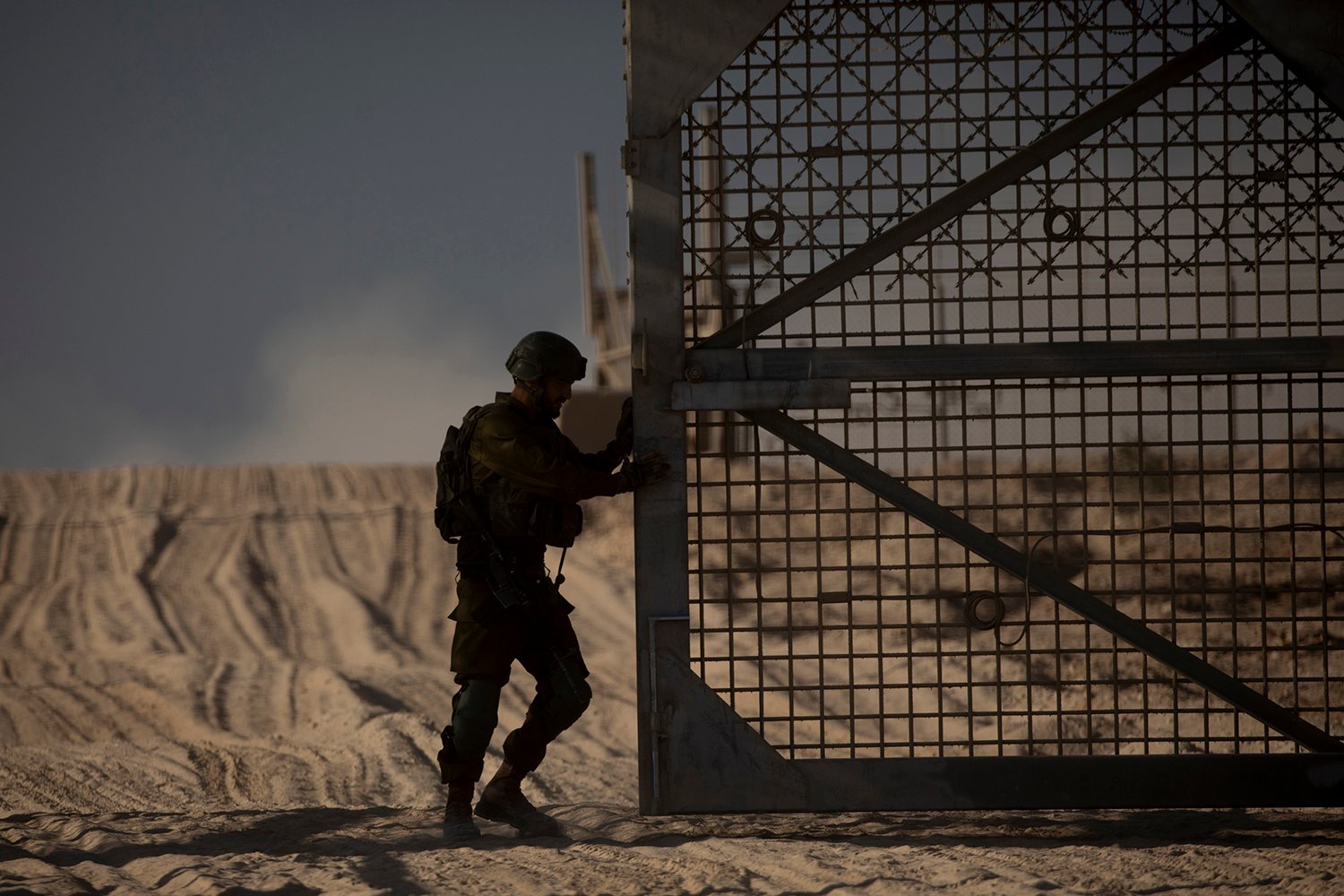 A soldier is silhouetted at a large border gate in front of a desert landscape.
