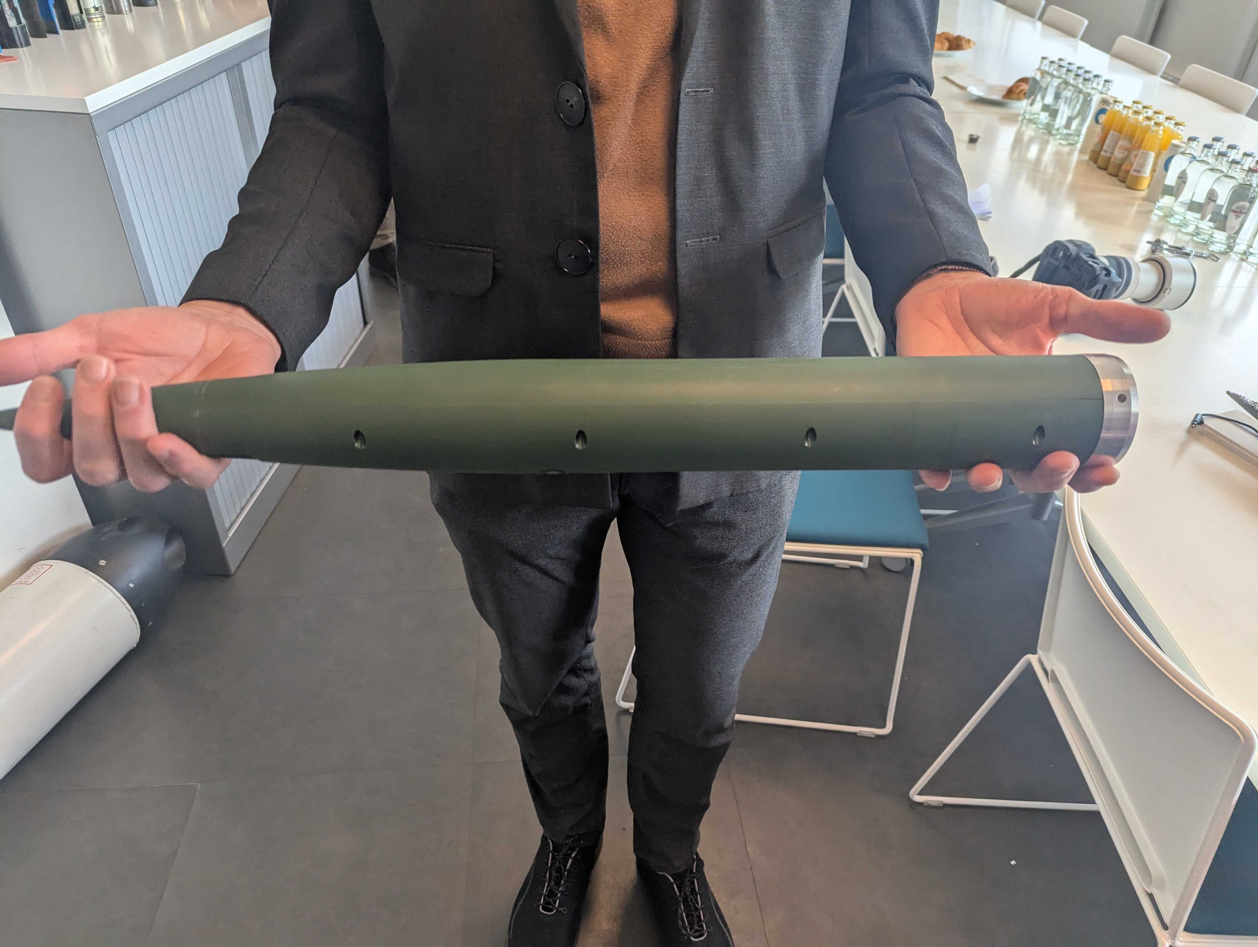 A man holds up a mock-up of a rocket warhead.