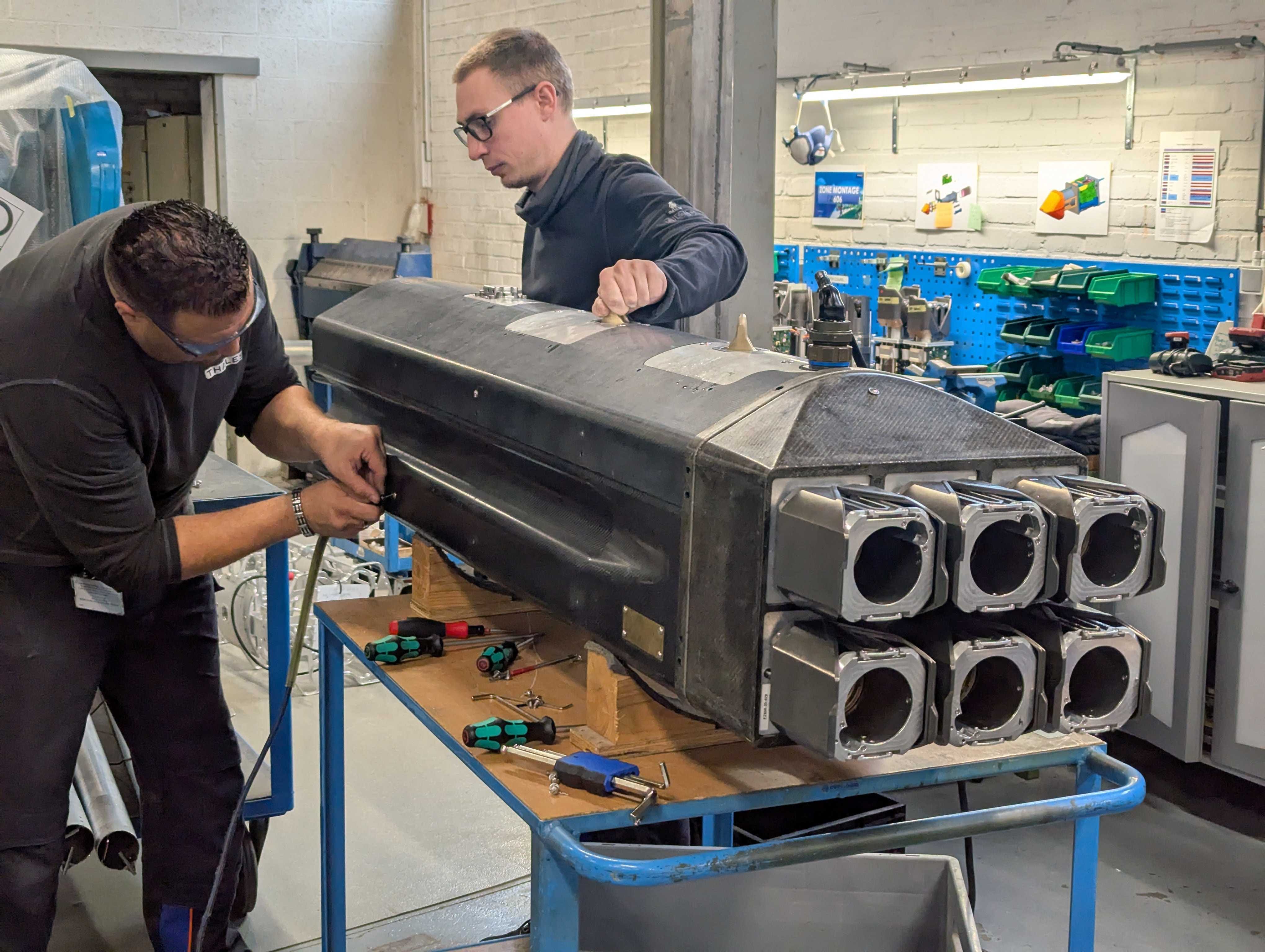 Two employees work on a 70mm multibarrel rocket launcher in a workshop.