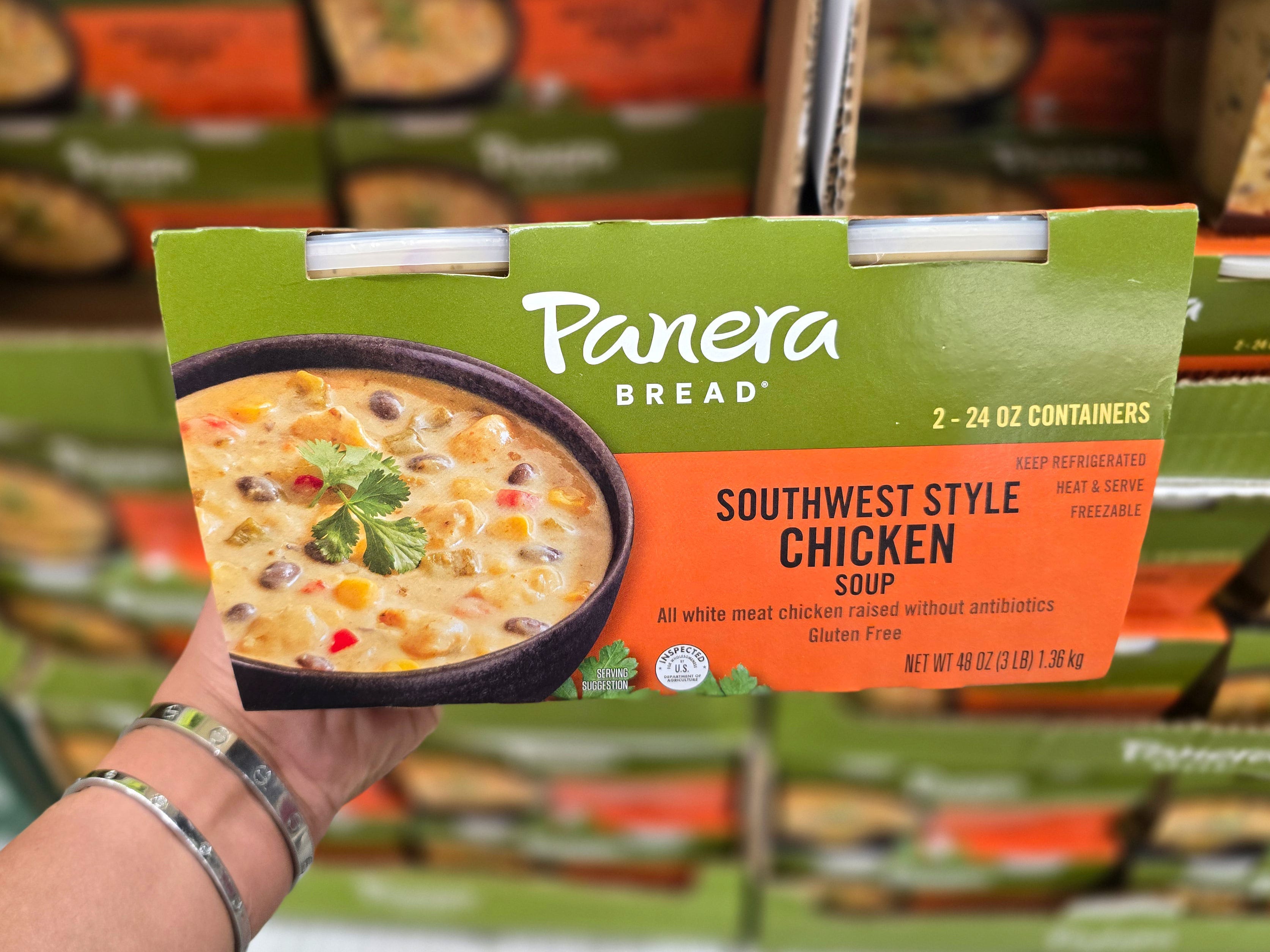 A hand holding a box of Panera Bread Southwest-style chicken soups.