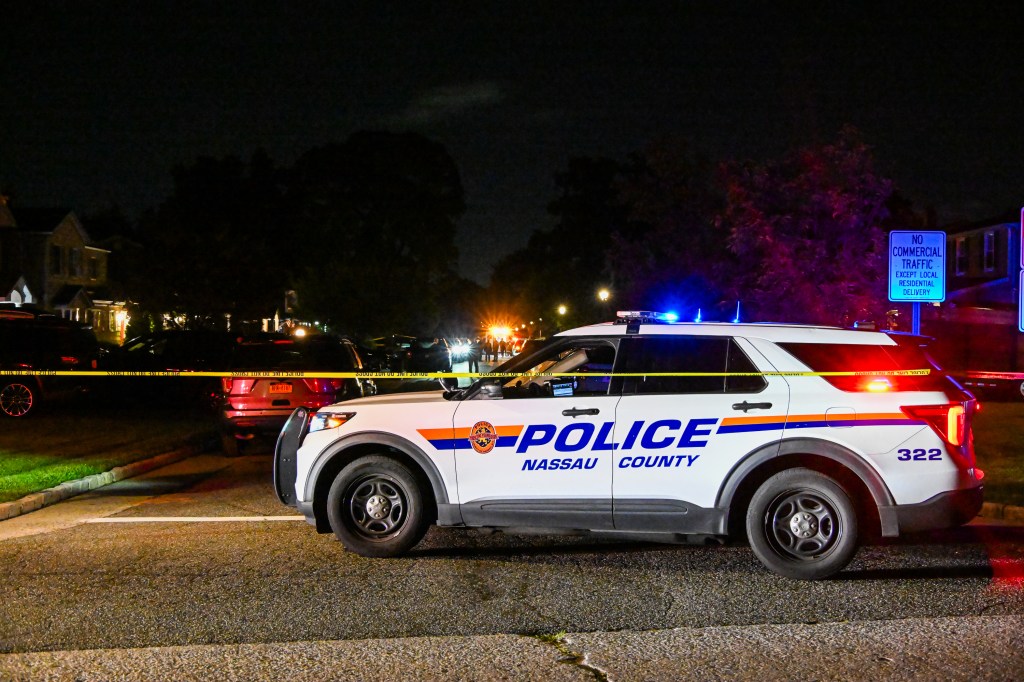 Nassau County Police vehicle with emergency lights on at night, with crime scene tape visible.