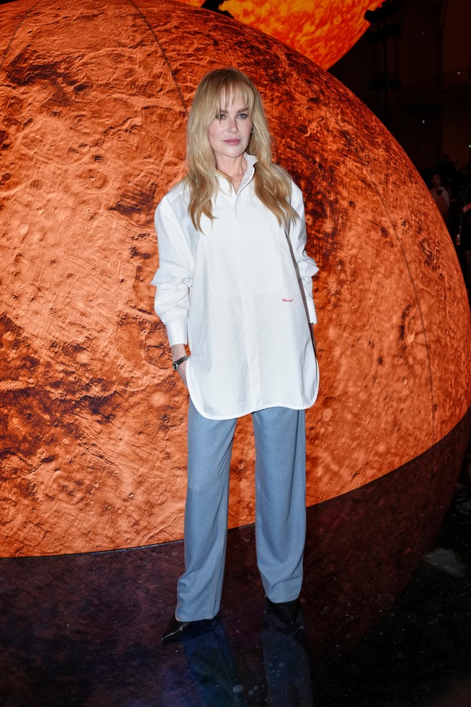 Nicole Kidman posing in a white button-down shirt and light blue pants.