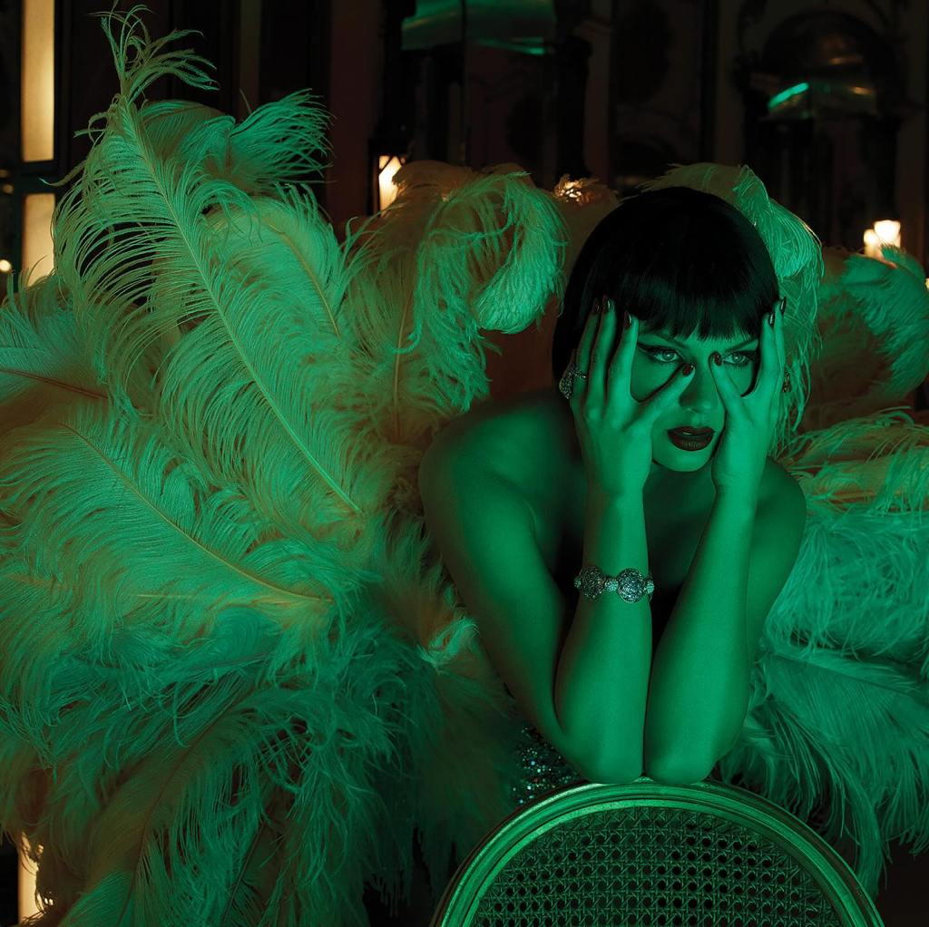A showgirl in heavy makeup and dark bobbed hair, wearing an ornate feather costume, with hands on her face.