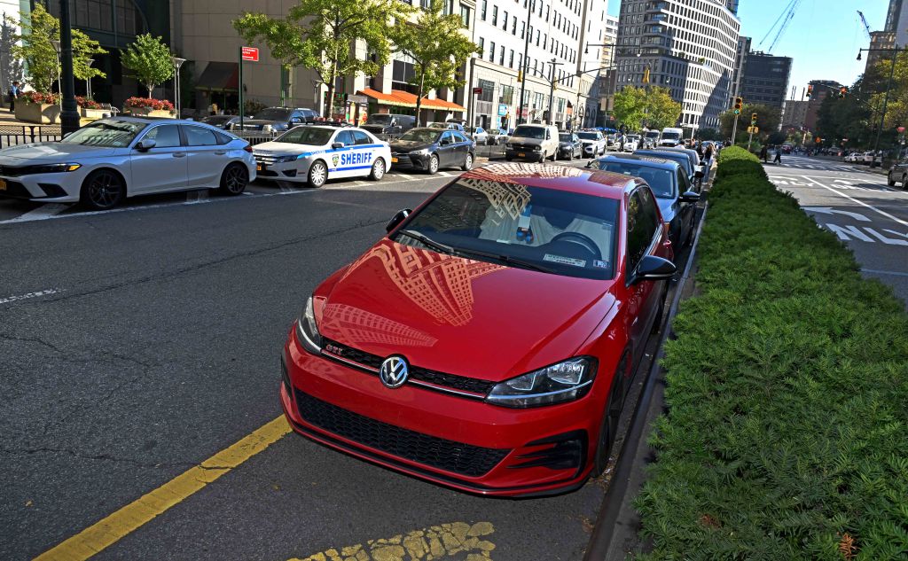 Red Volkswagen parked on a city street, with a white Sheriff patrol car and other vehicles behind it.