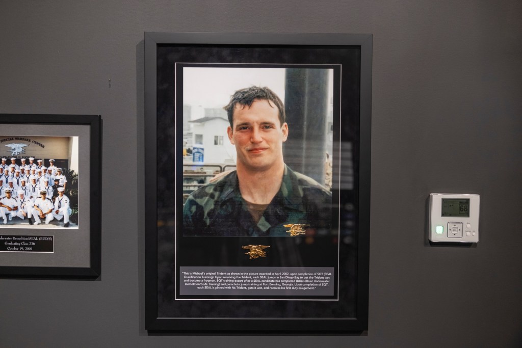 A framed portrait of Michael Murphy in a military uniform, with a gold SEAL Trident pin on the bottom left of the photo.