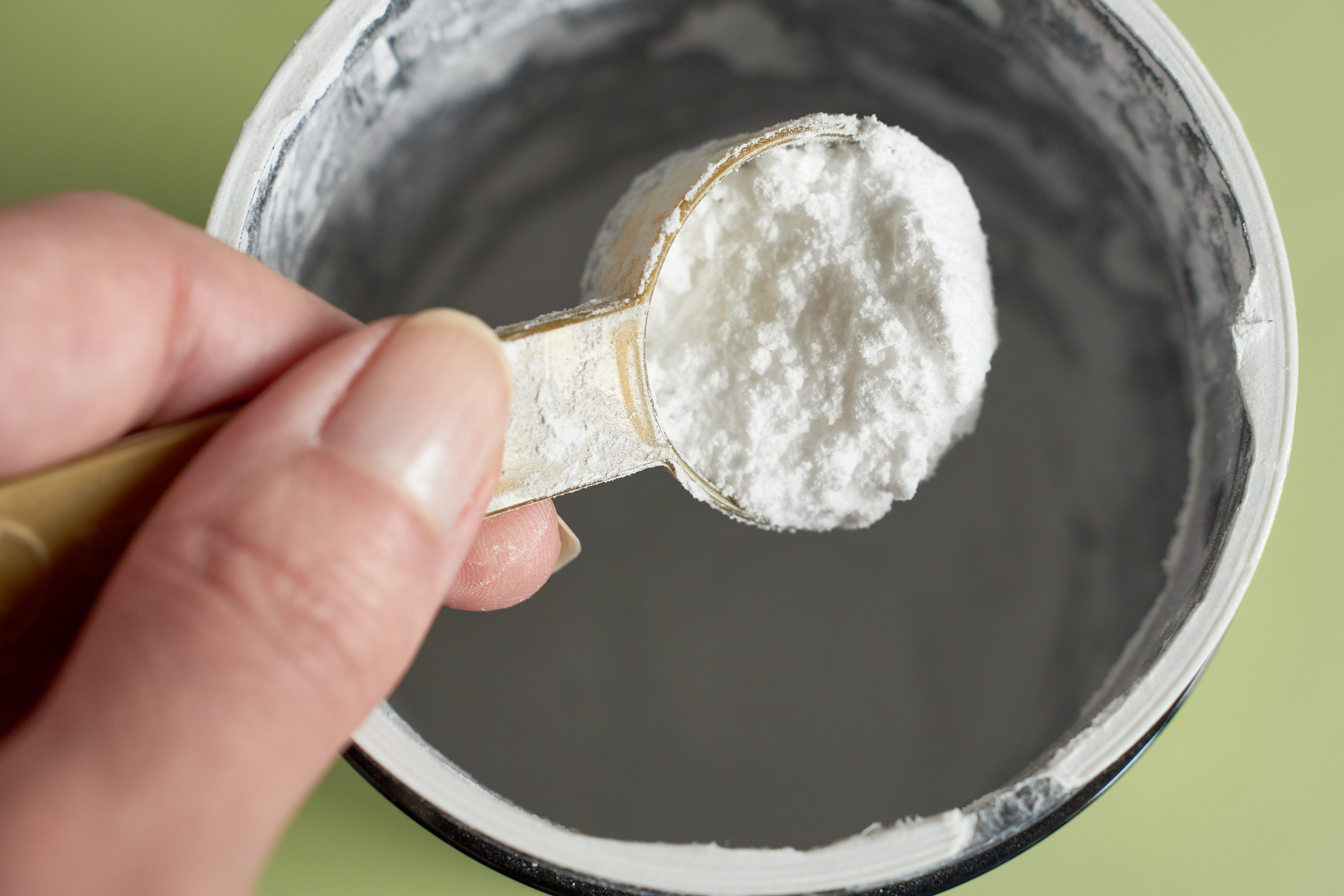 A hand holding a scoop of creatine powder.