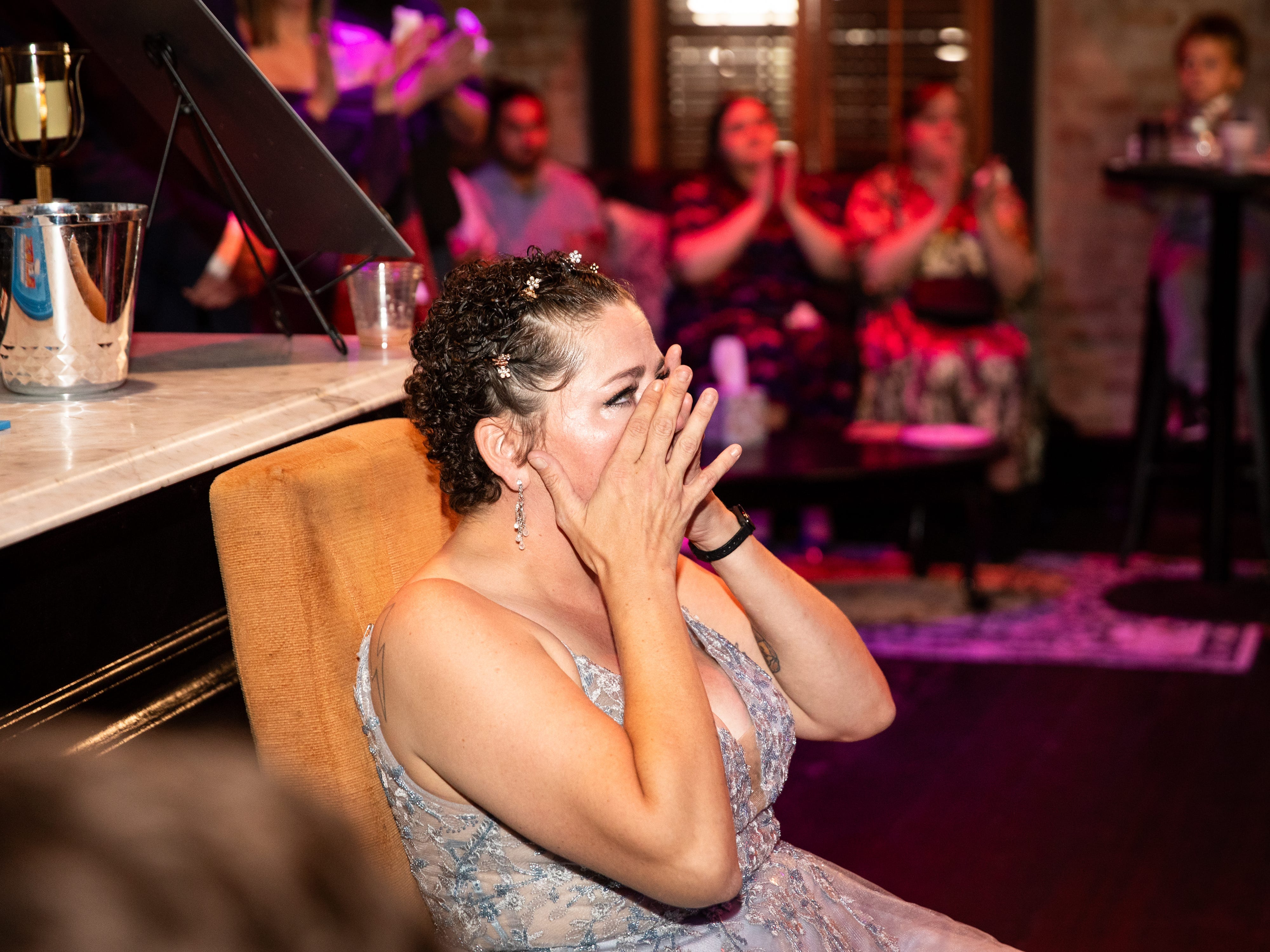 A woman in a silver dress with her hands clasped over her face