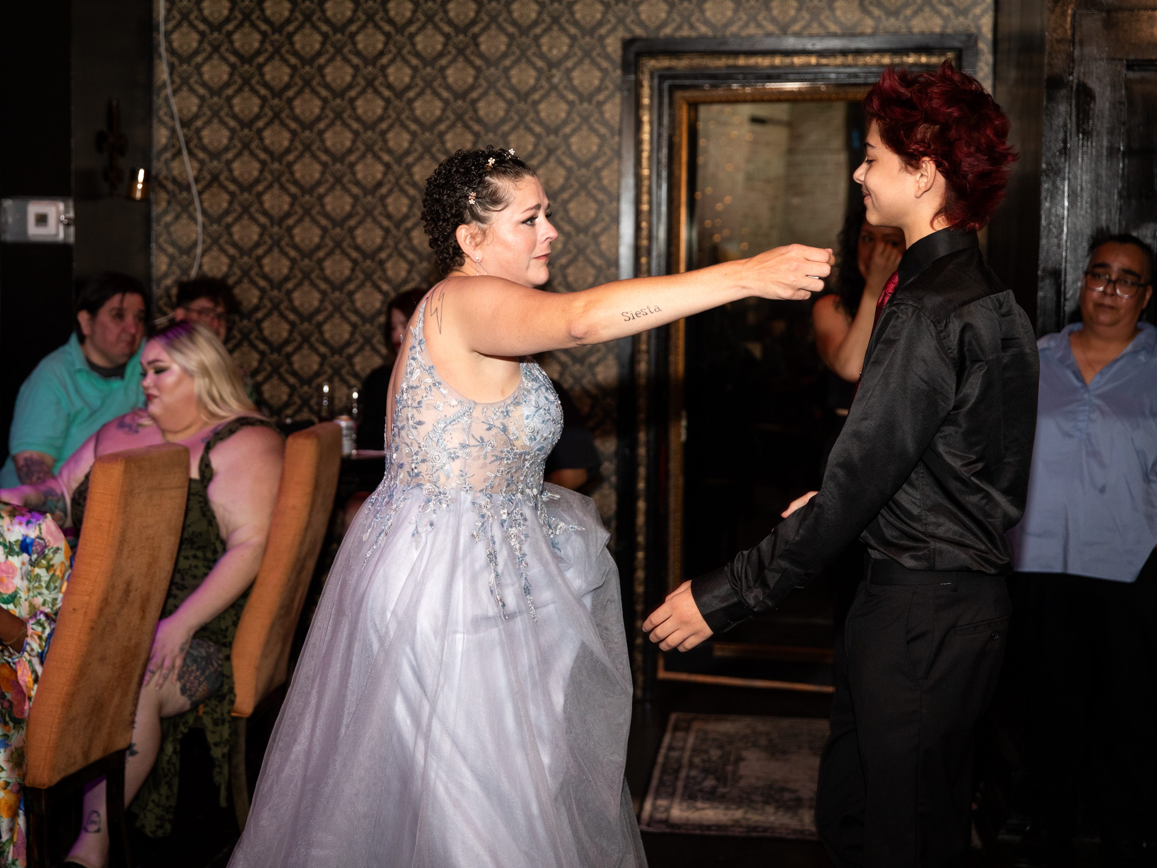 A mom in a silver dress tenderly reaches out to her son