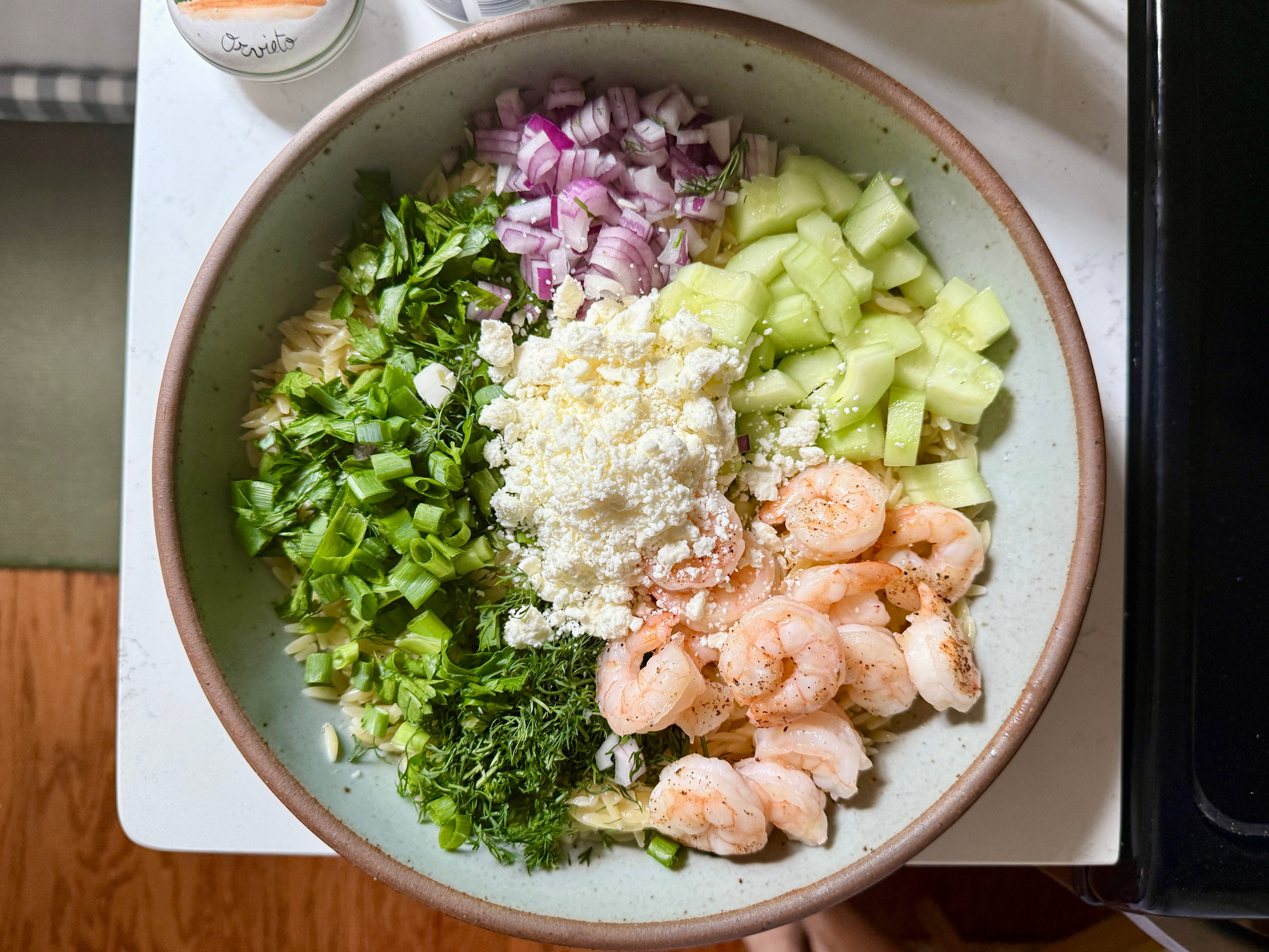 Chopped ingredients on a bed of orzo in a bowl.