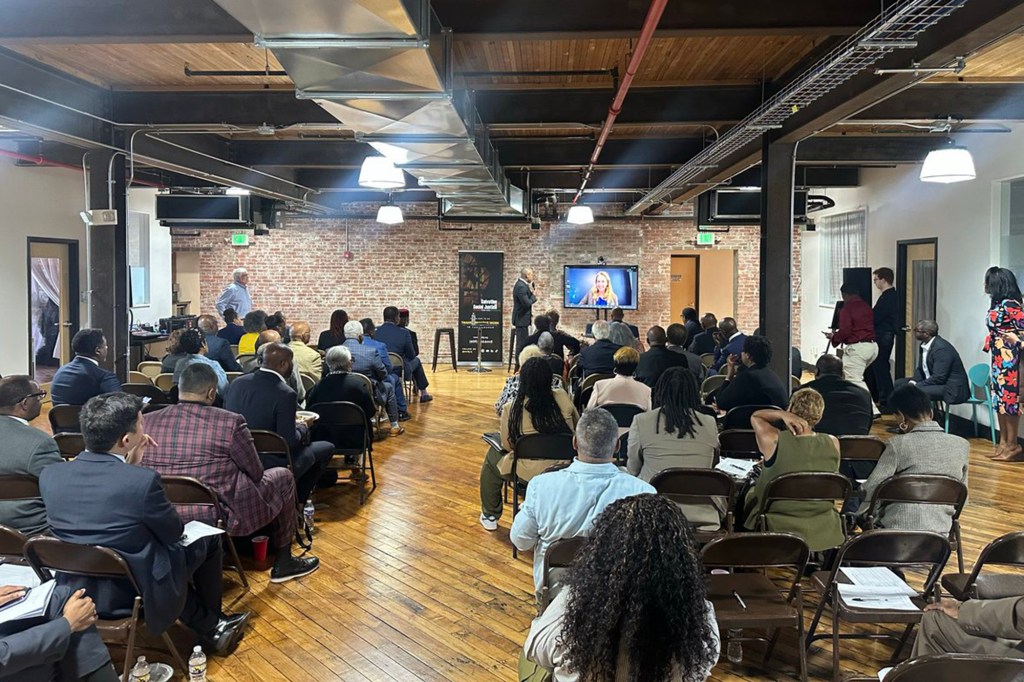 A room full of attendees facing a screen showing Mikie Sherrill speaking virtually.