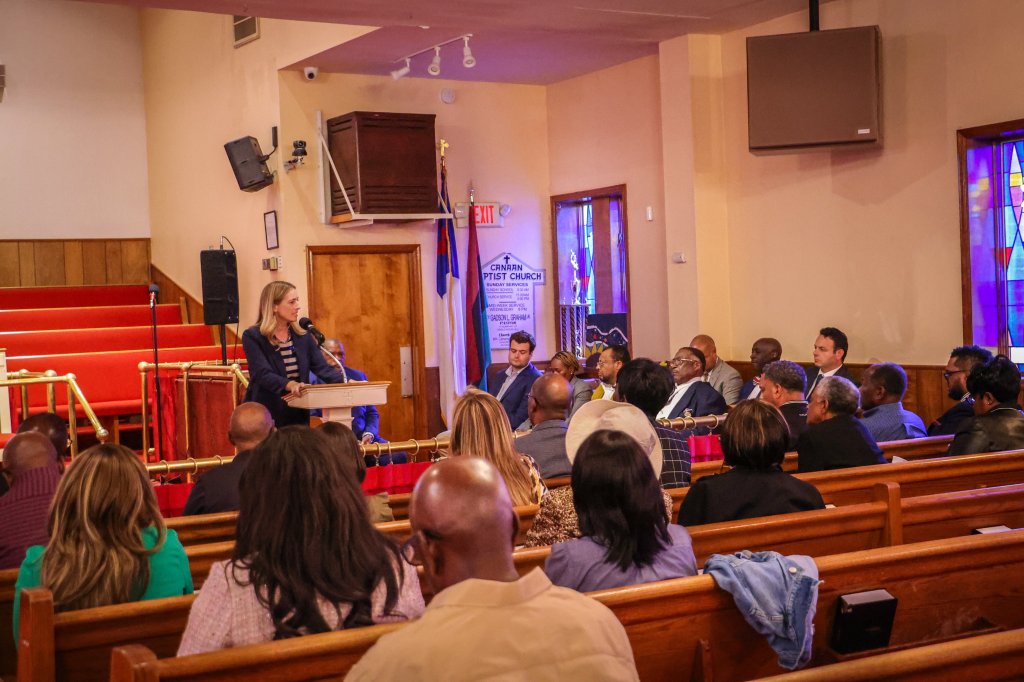 Mikie Sherrill speaking at a podium in Canaan Baptist Church to a seated audience.