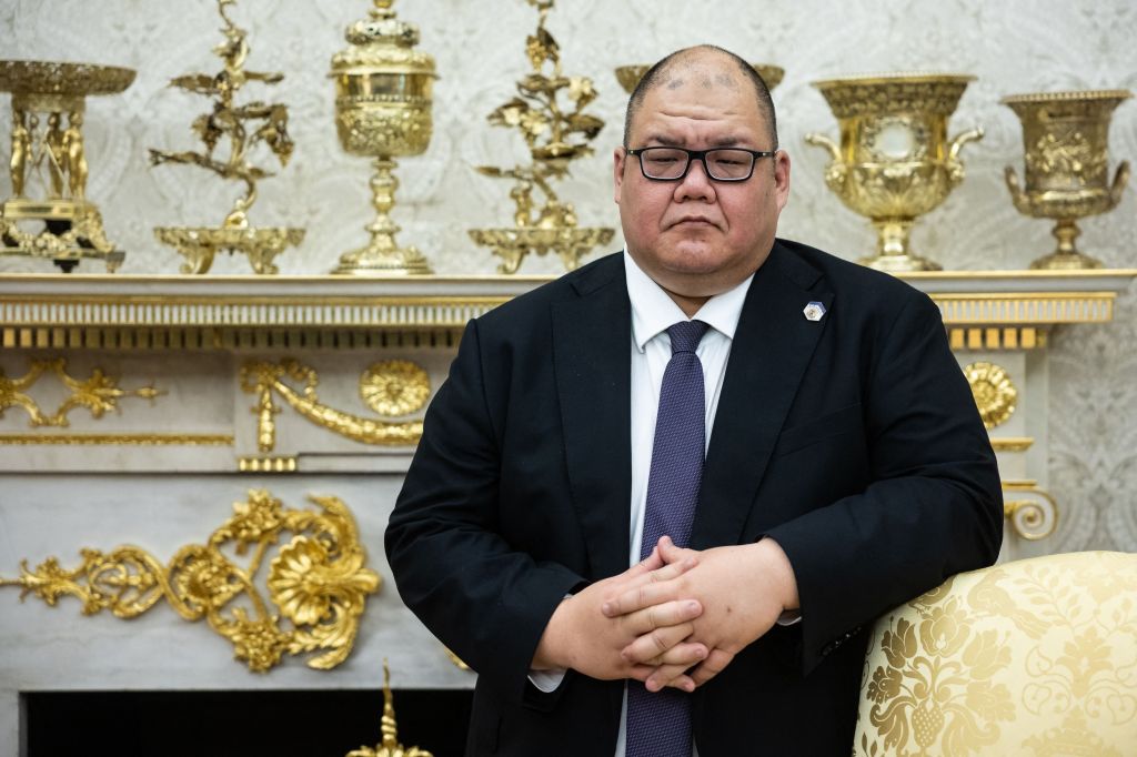 Man in a suit and tie standing in front of a golden fireplace.
