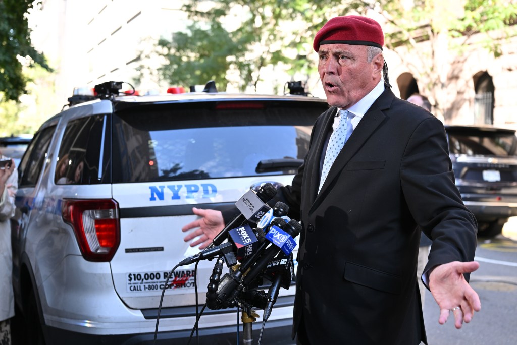 Curtis Sliwa, Republican mayoral nominee, speaking at a press conference with an NYPD vehicle and multiple news microphones visible.