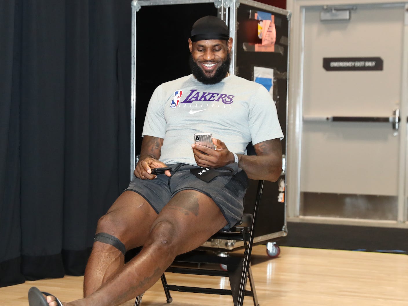LeBron James smiles while sitting in a chair and looking at his phone.