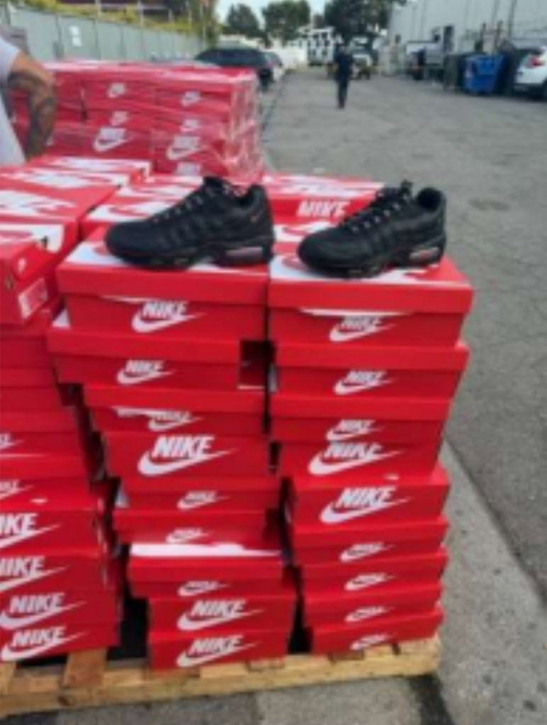 Numerous red Nike shoe boxes stacked with two black Nike sneakers on top.