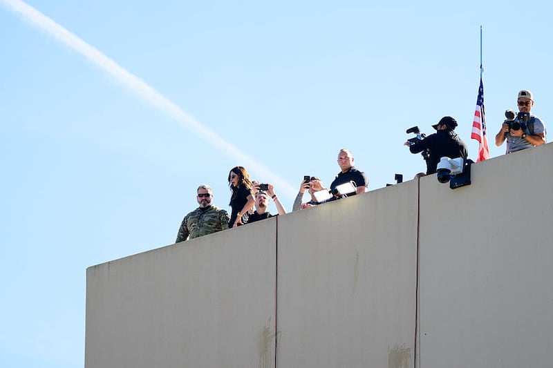 PORTLAND, OREGON - OCTOBER 7:  U.S. Homeland Security Secretary Kristi Noem observes the scene of ongoing protests at the Immigration and Customs Enforcement (ICE) facility on October 7, 2025 in Portland, Oregon. Secretary Noem arrived in Portland on Tuesday to meet with law enforcement amidst a dispute between the Trump administration and Oregon officials about deploying the National Guard to the state. Also pictured is conservative influencer Nick Sortor (3rd L).