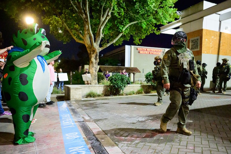 Protester in forg constume faces Federal agents at an Immigration and Customs Enforcement (ICE) facility in downtown Portland, Oregon, on October 6, 2025.