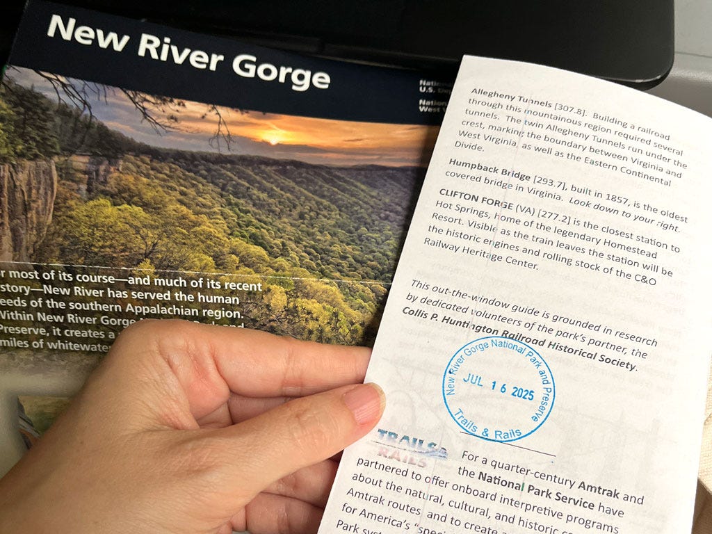 A hand holding a pamphlet for the Amtrak Trails and Rails program over one about New River Gorge National Park.