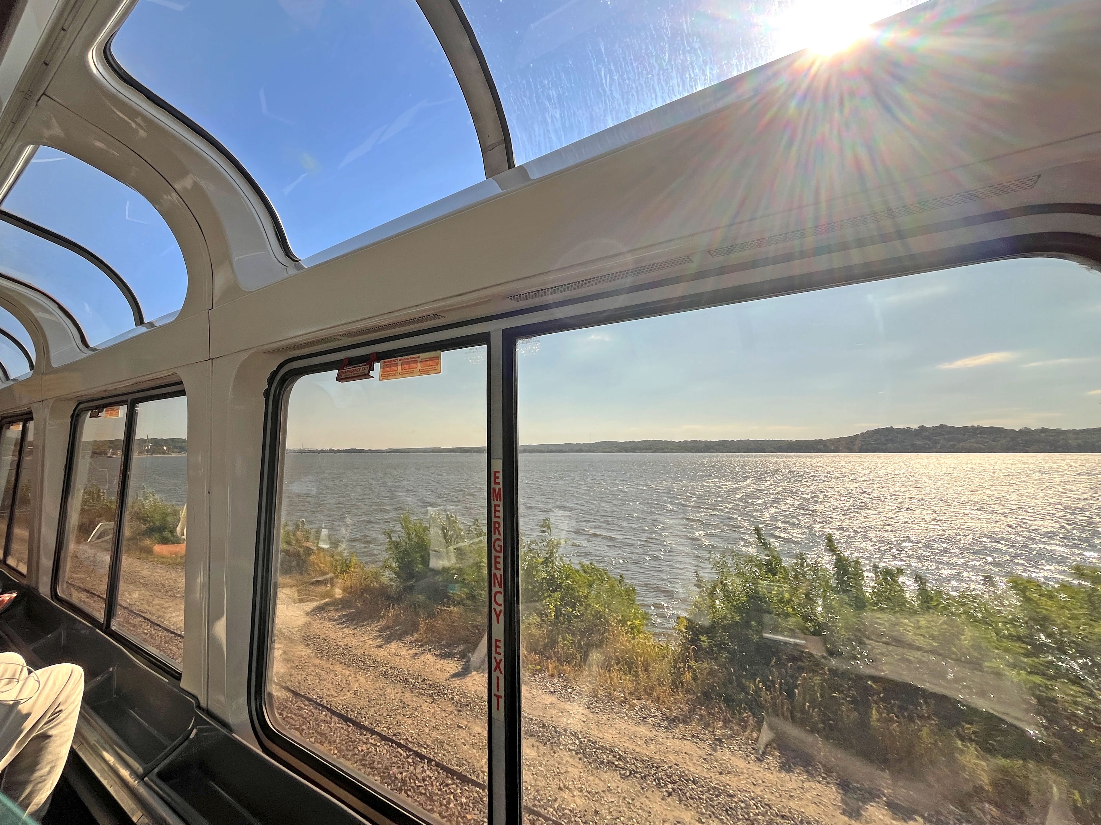 The view of a large body of water from a train car with floor-to-ceiling windows.