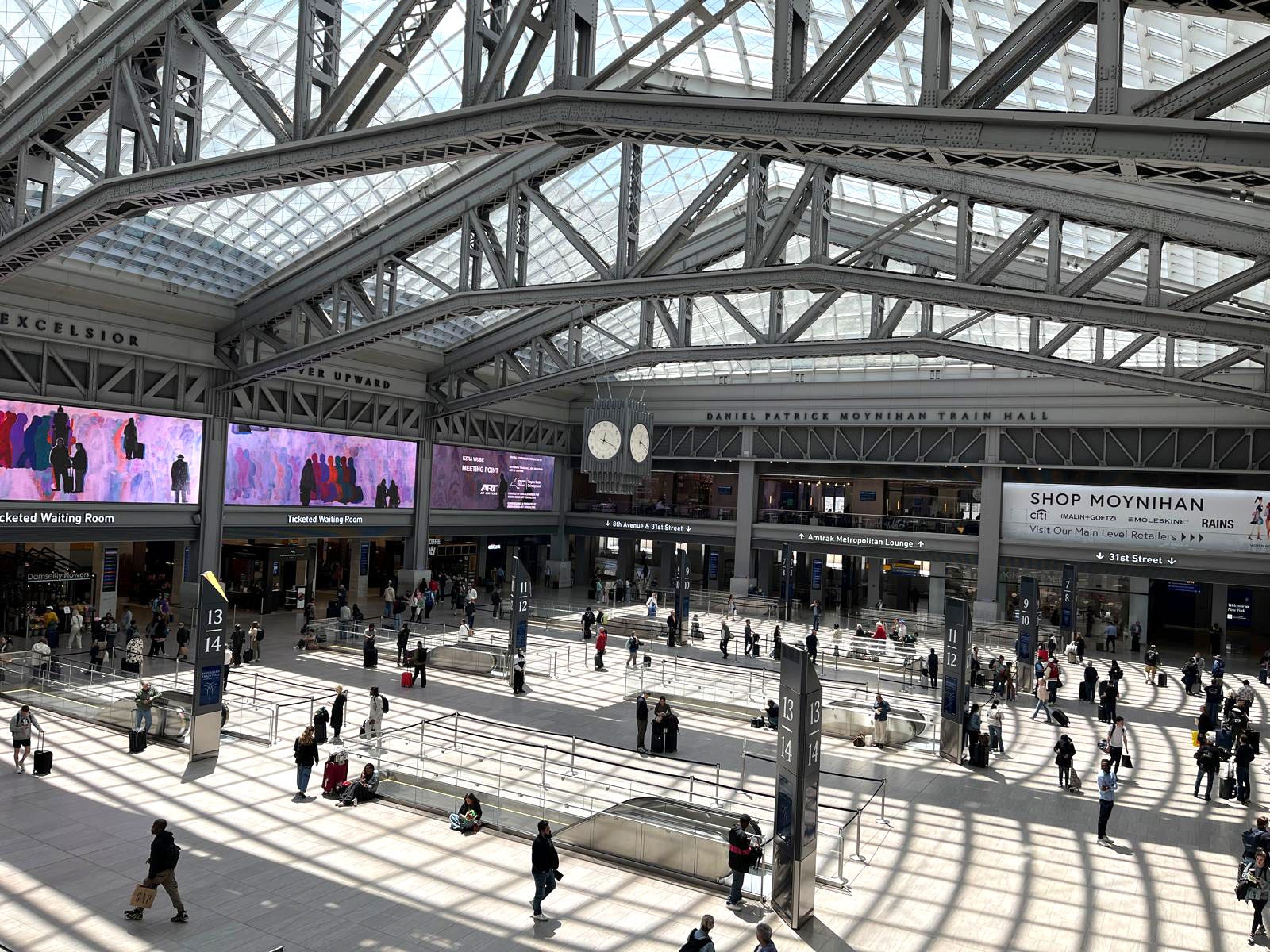The inside of a busy train hall with shadows on the ground from the skylights.