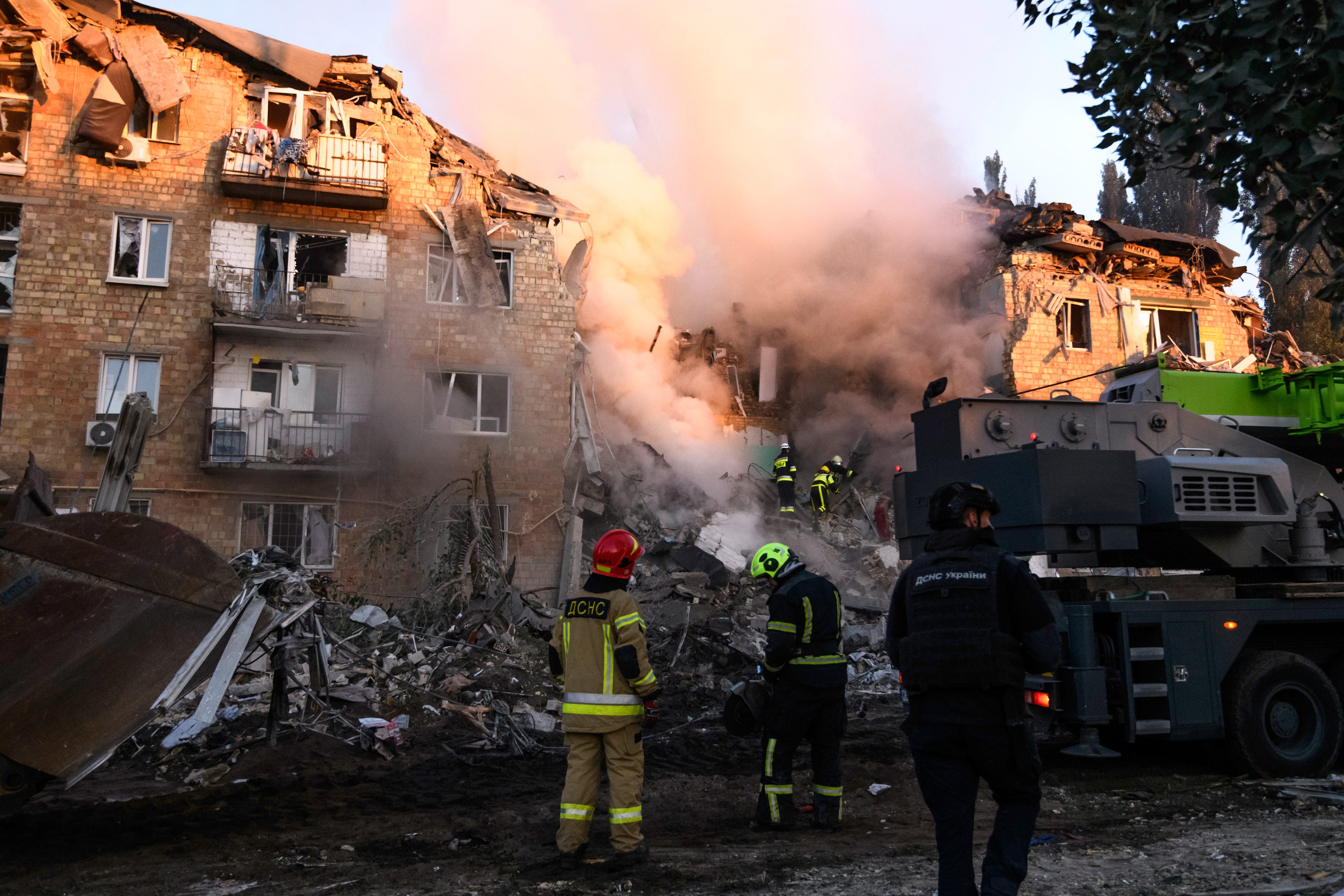 A collpased building with lots of smoke with emergency workers looking on