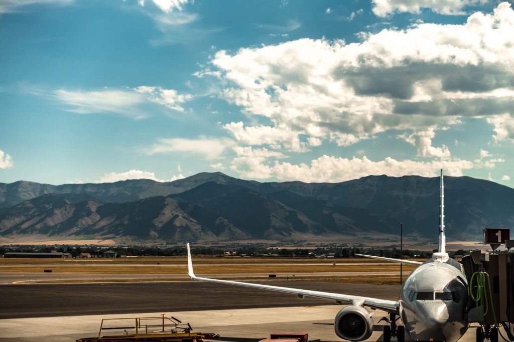 Bozeman Montana airport with an airplane at the gate and Rocky Mountains in the background.