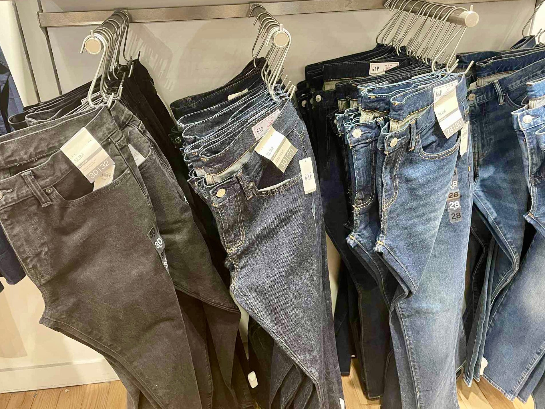 Pairs of jeans in a row hung up on hooks.