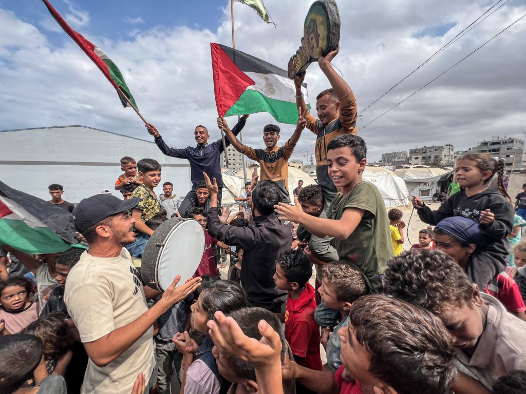 Palestinians in Nusairat Camp celebrating a new Gaza ceasefire deal, with people waving flags and holding a drum.