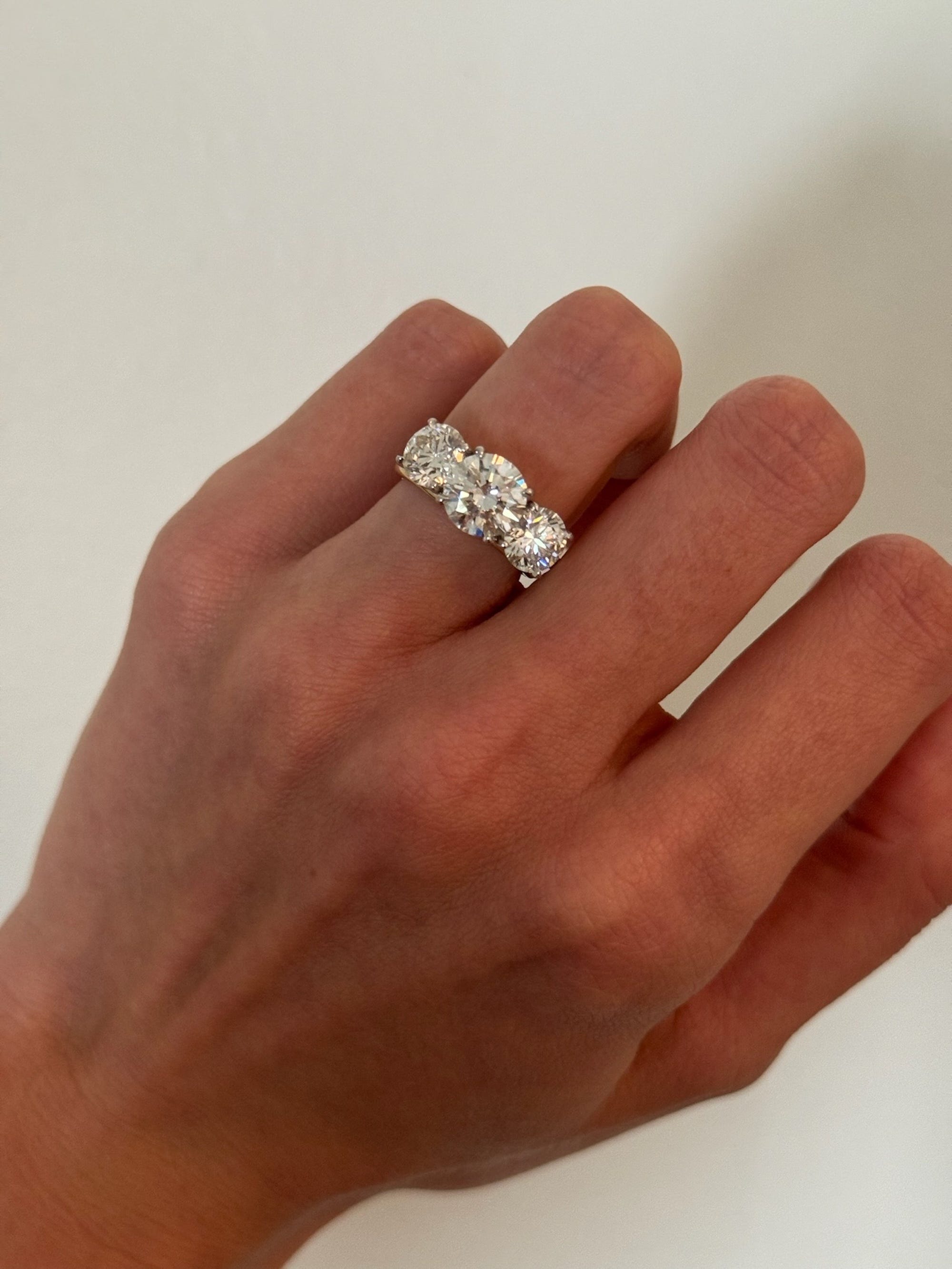 An engagement ring with three diamonds sits on a hand.