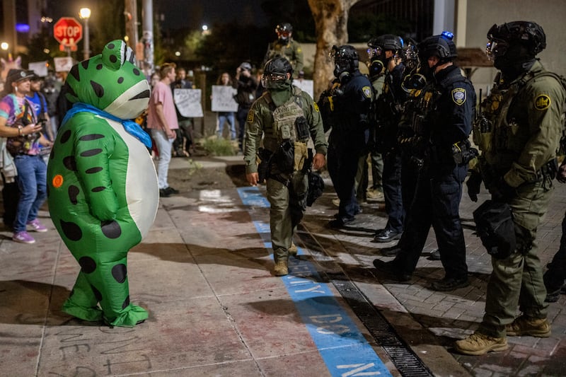 A protester in a frog costume stands in front of a line of federal law enforcement officers outside a United States Immigration and Customs Enforcement (ICE) facility in Portland