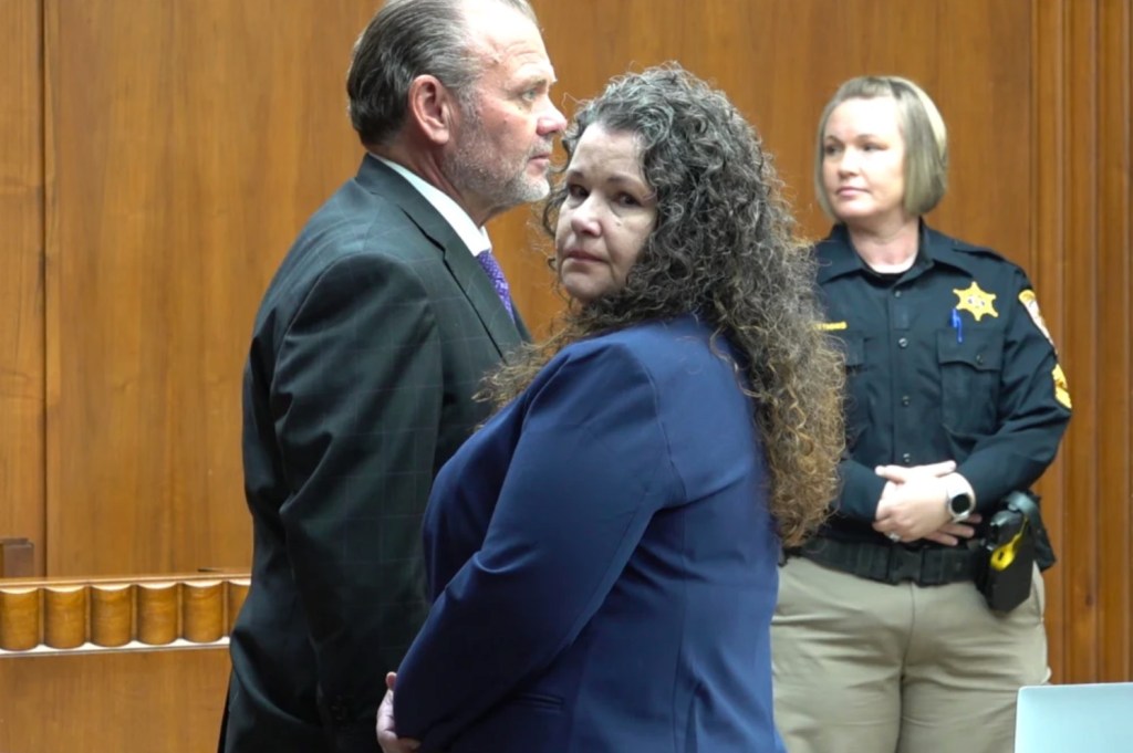 Sarah Hartsfield in a courtroom, with a man in a suit beside her and a female officer behind her.