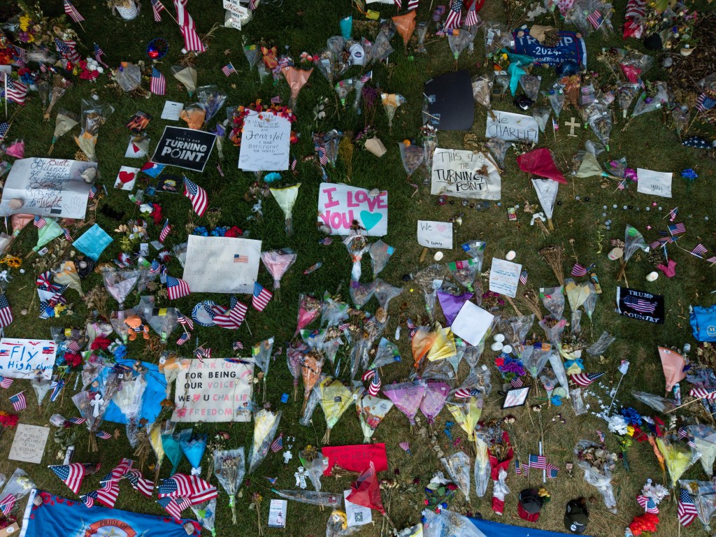 A memorial for conservative commentator Charlie Kirk at Utah Valley University, with flowers, small American flags, and handwritten signs.