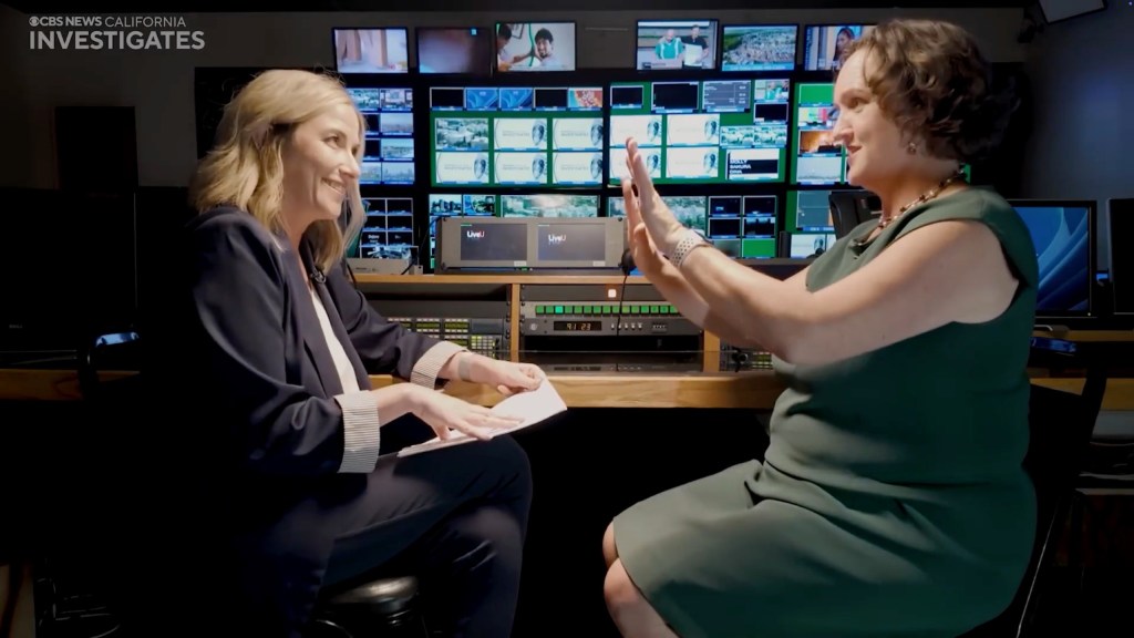 Former Rep. Katie Porter appearing on a CBS News interview with reporter Julie Watts, with multiple screens in the background.