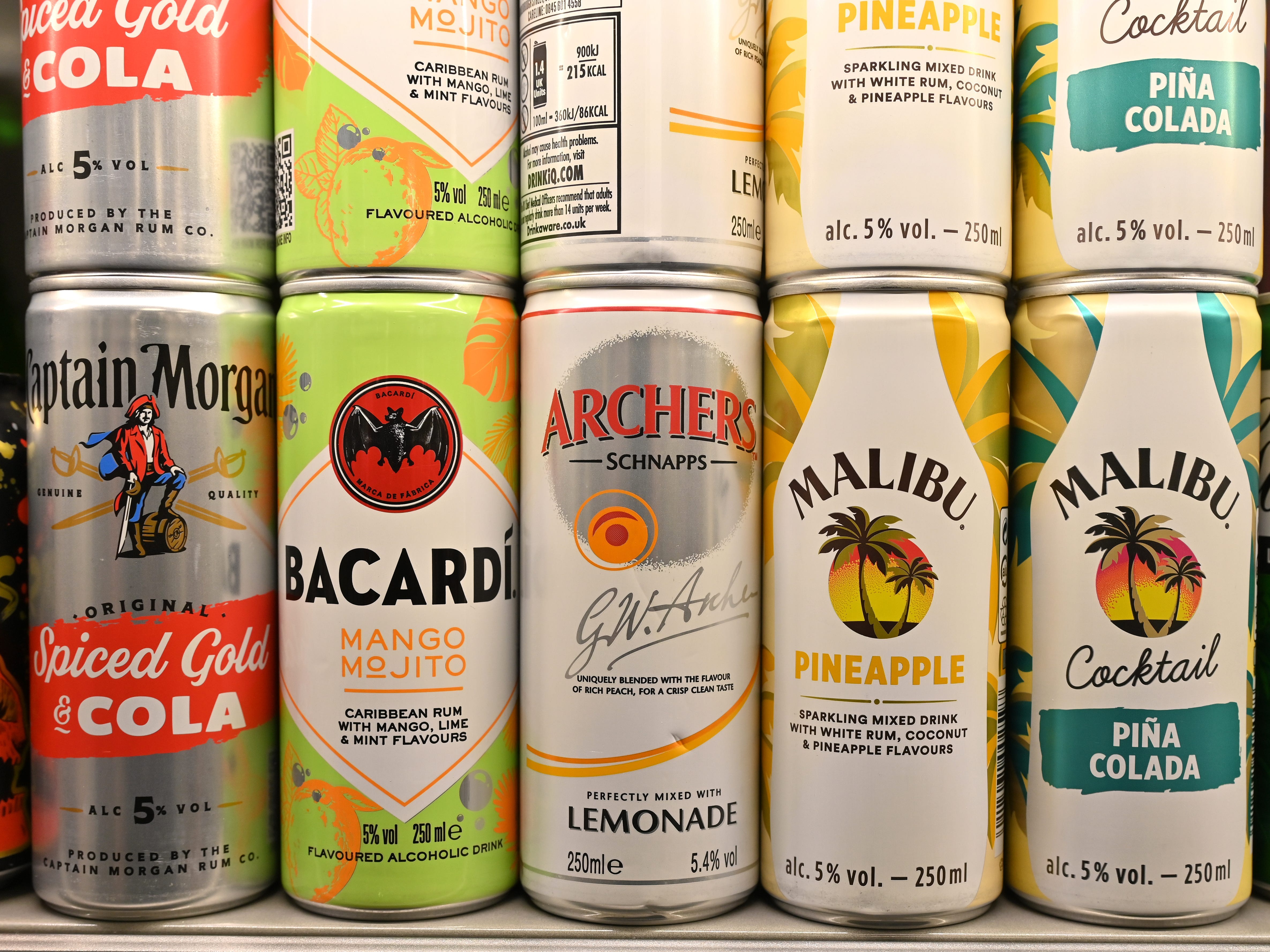 Various cans of alcoholic ready-to-drink beverages including Captain Morgan Rum and Coke, Bacardi MoJito, Archers and Lemonade, Malibu and Pineapple, Pina Colada Cocktail and Gordon's Gin and Tonic are displayed for sale in a supermarket.