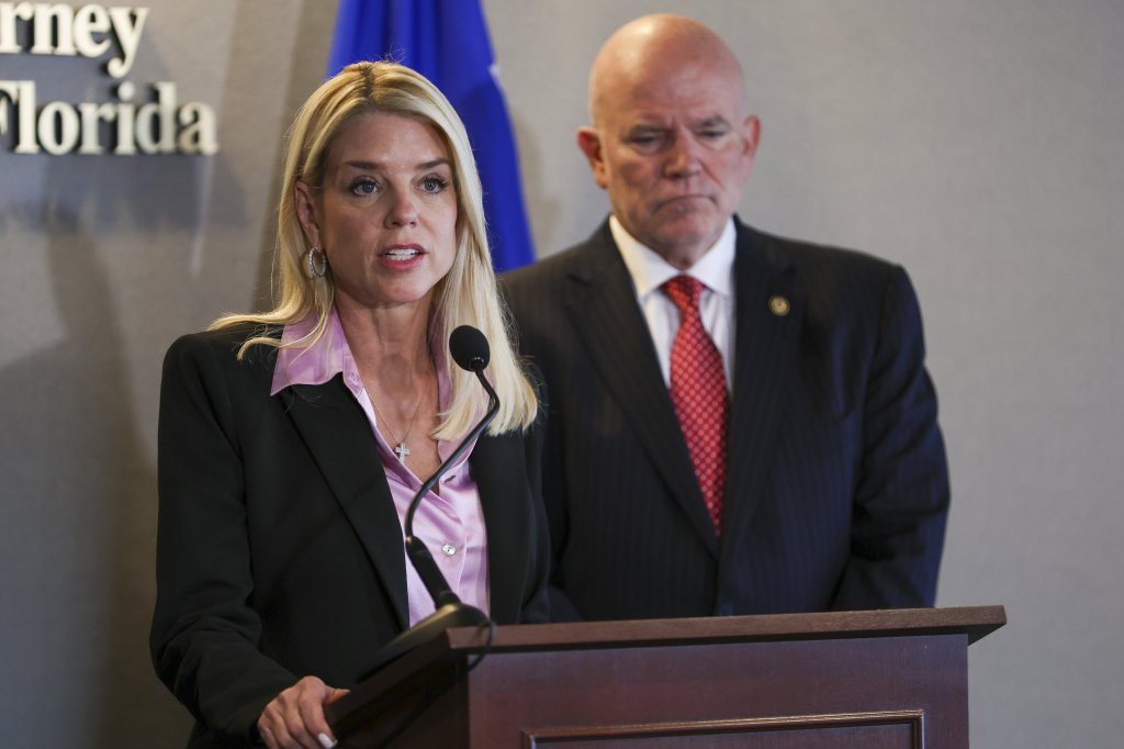 United States Attorney General Pam Bondi speaking at a press conference next to a man in a suit.