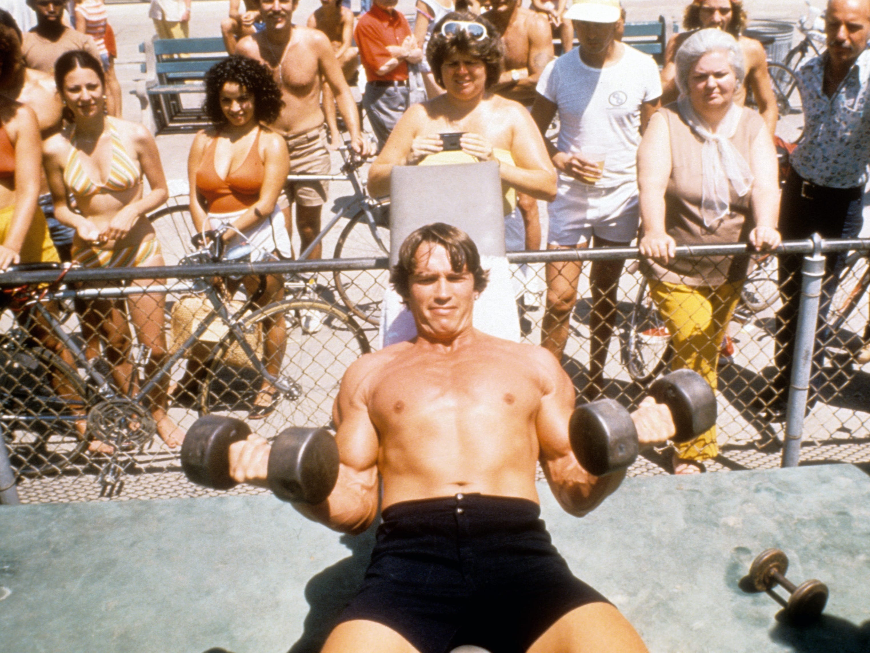 Schwarzenegger lifting free weights on a beach.