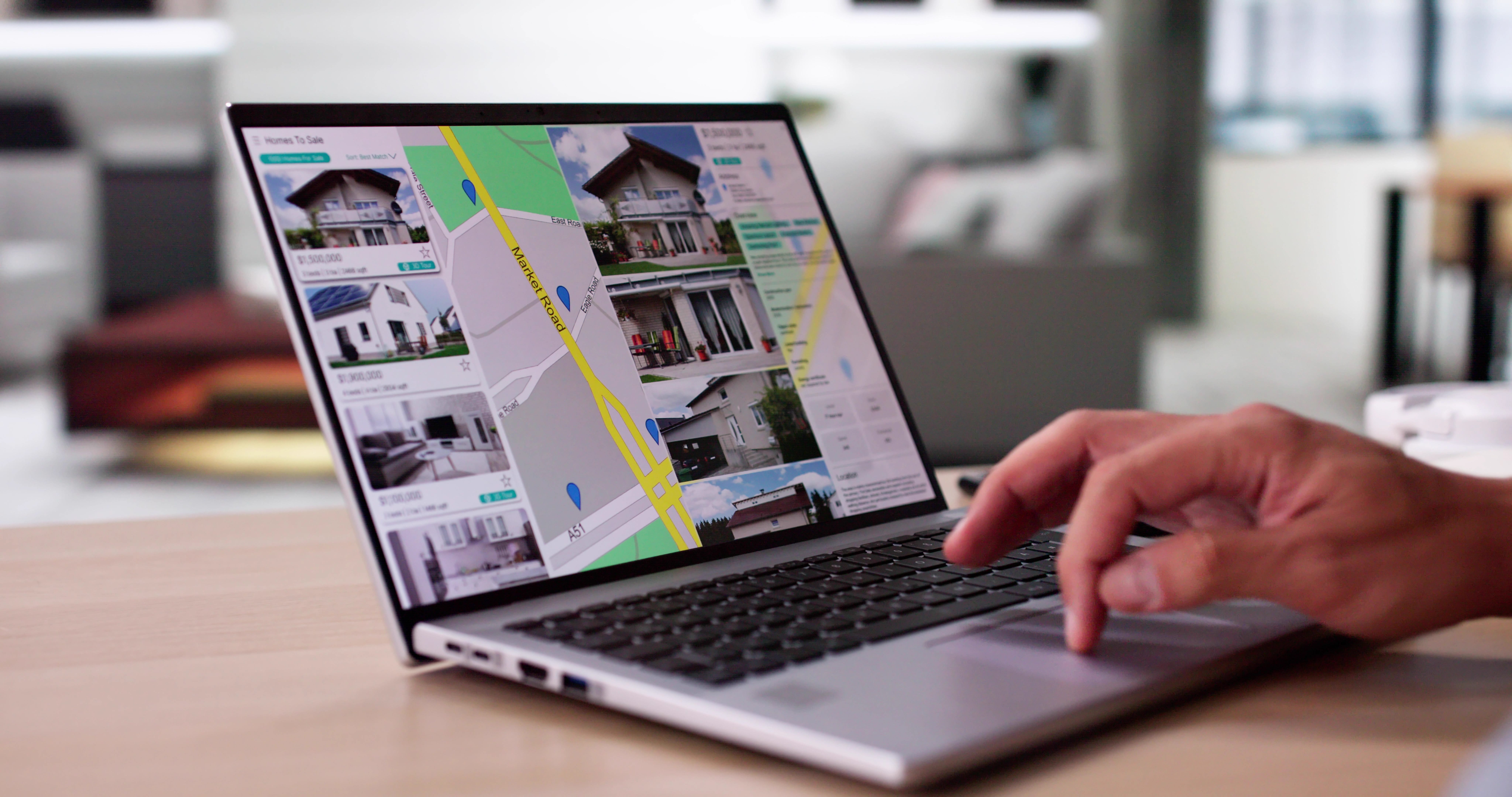 A hand hovering next to a laptop with several home listings featured.