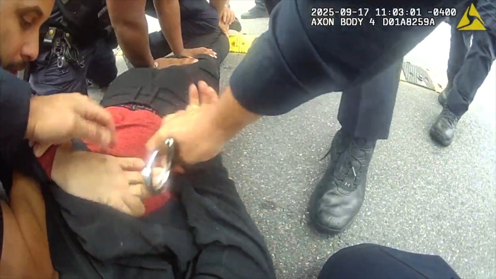 A person in black and red clothing being handcuffed on the ground by police officers.