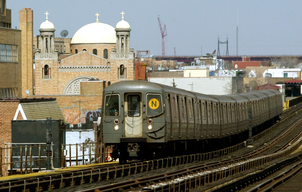 A subway train traveling above ground past a church.