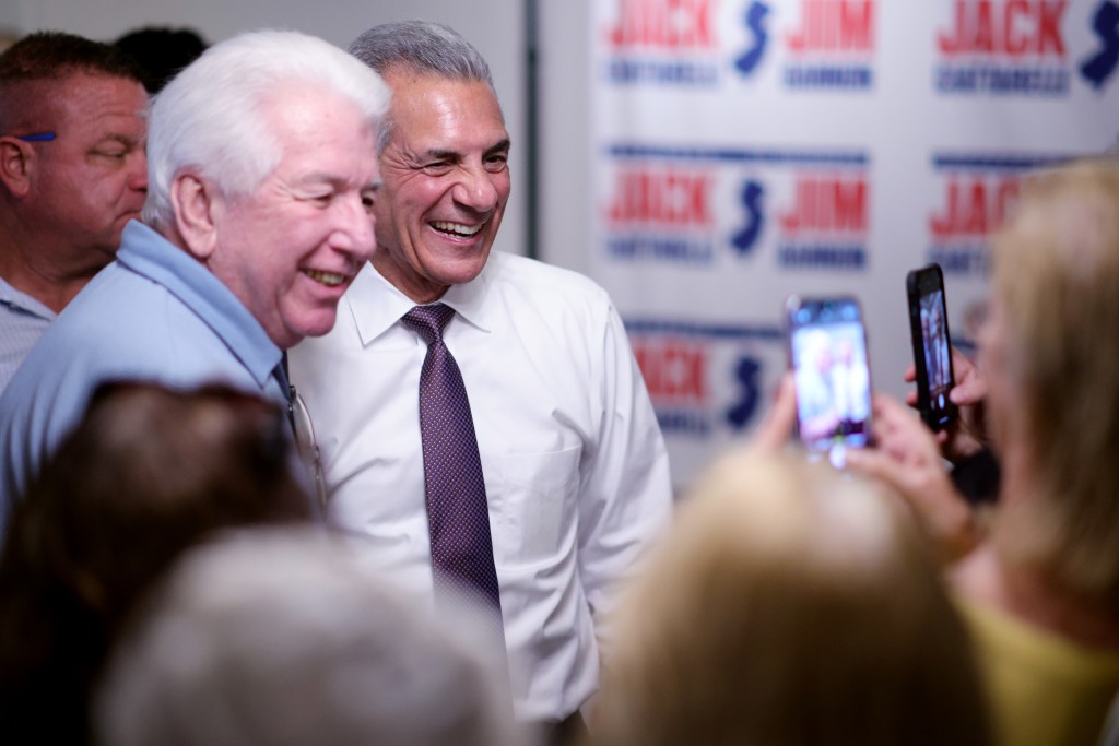 Republican candidate Jack Ciattarelli laughs with an older man, while people in the crowd take photos of them.