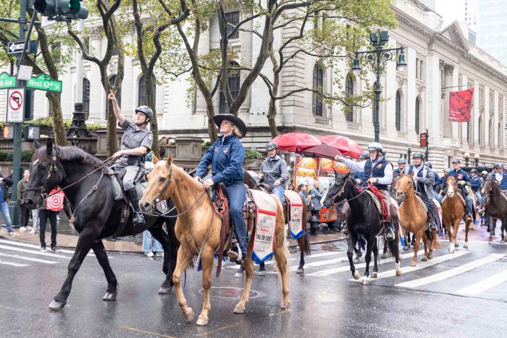 Riders on horseback, one in a police uniform, parading on a city street past a street sign for West 42nd St.