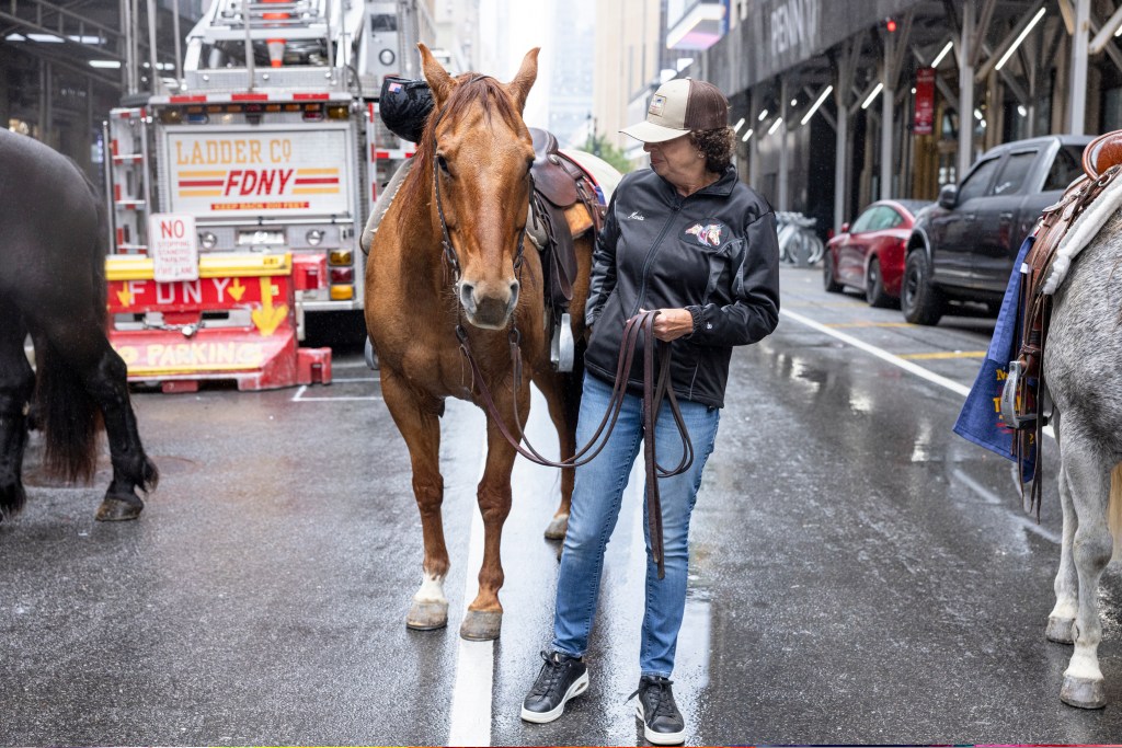 A woman in a baseball cap holding a horse's reins on a city street with an FDNY truck in the background.